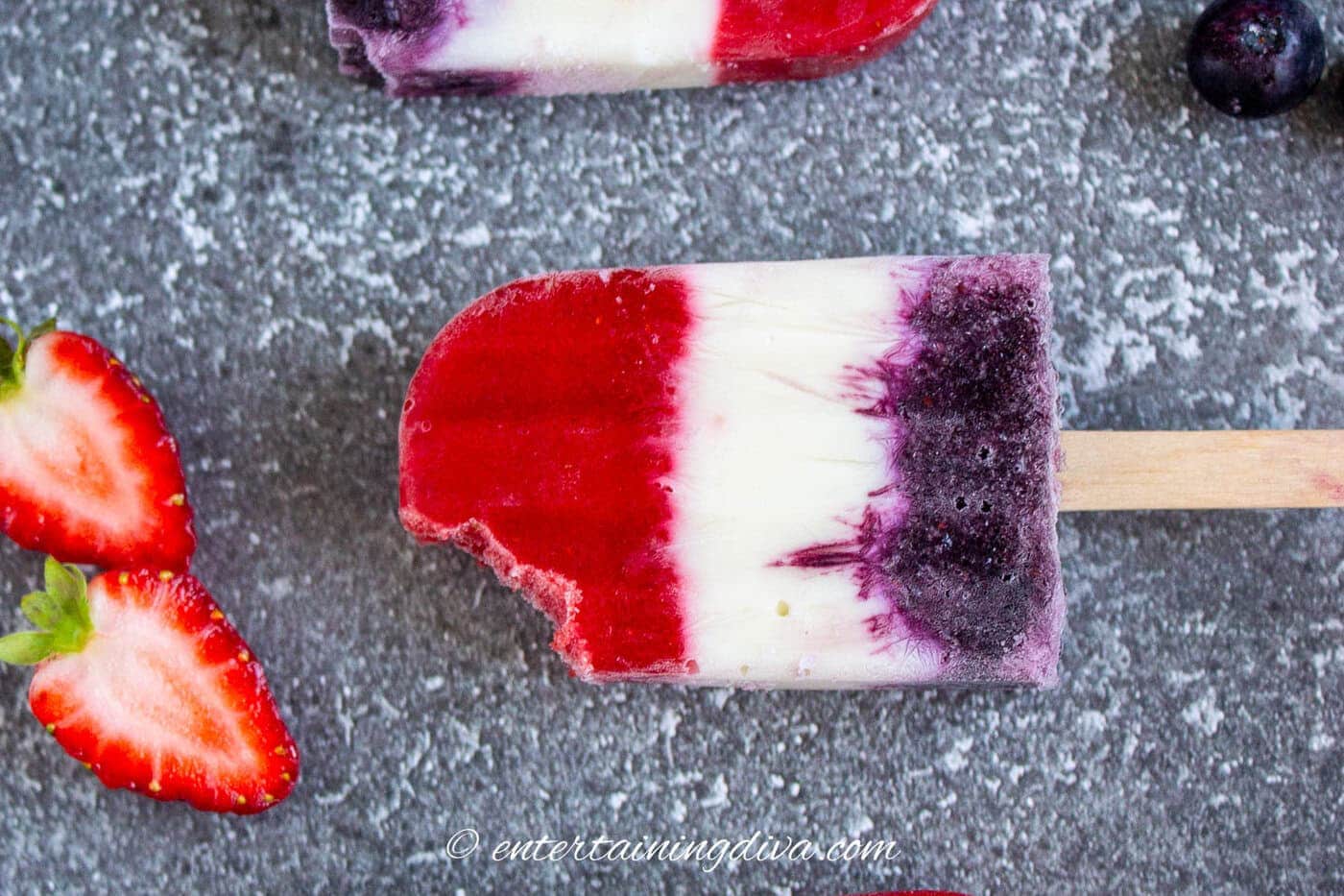 A red white and blue popsicle with sliced strawberries and blueberries on a countertop