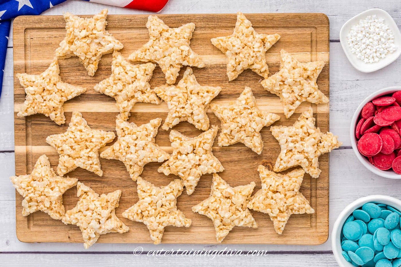 star-shaped rice krispie treats on a cutting board beside bowls with red and blue candy melts and white star sprinkles