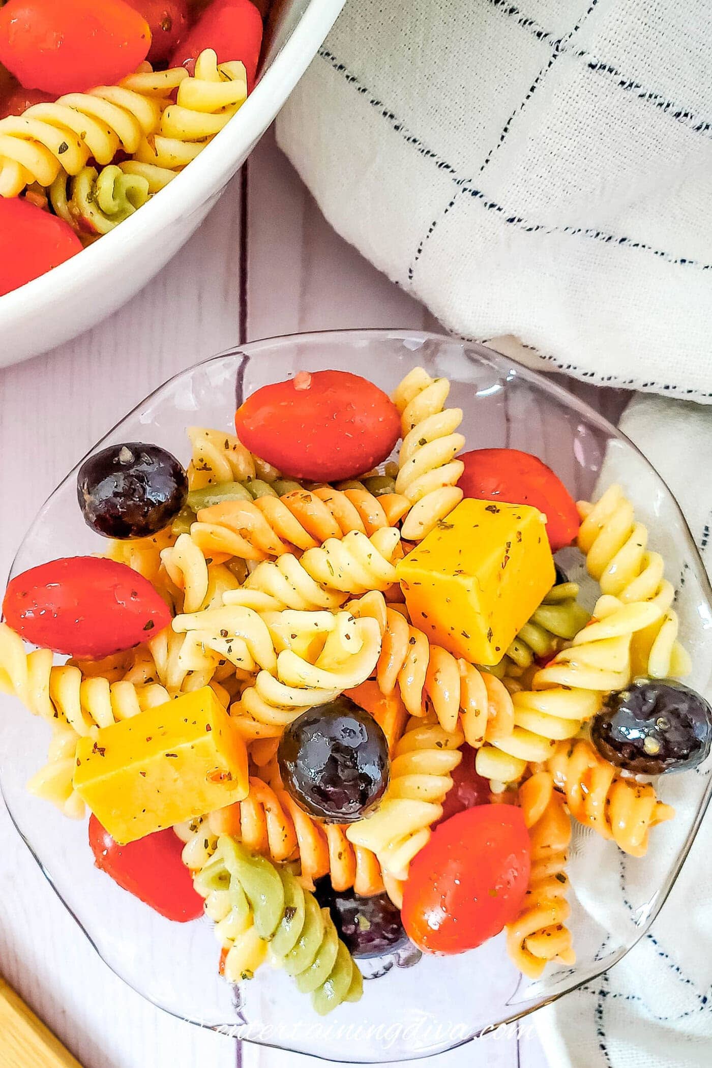 A bowl of tri-color rotini pasta salad with olives, tomatoes and cheddar cheese