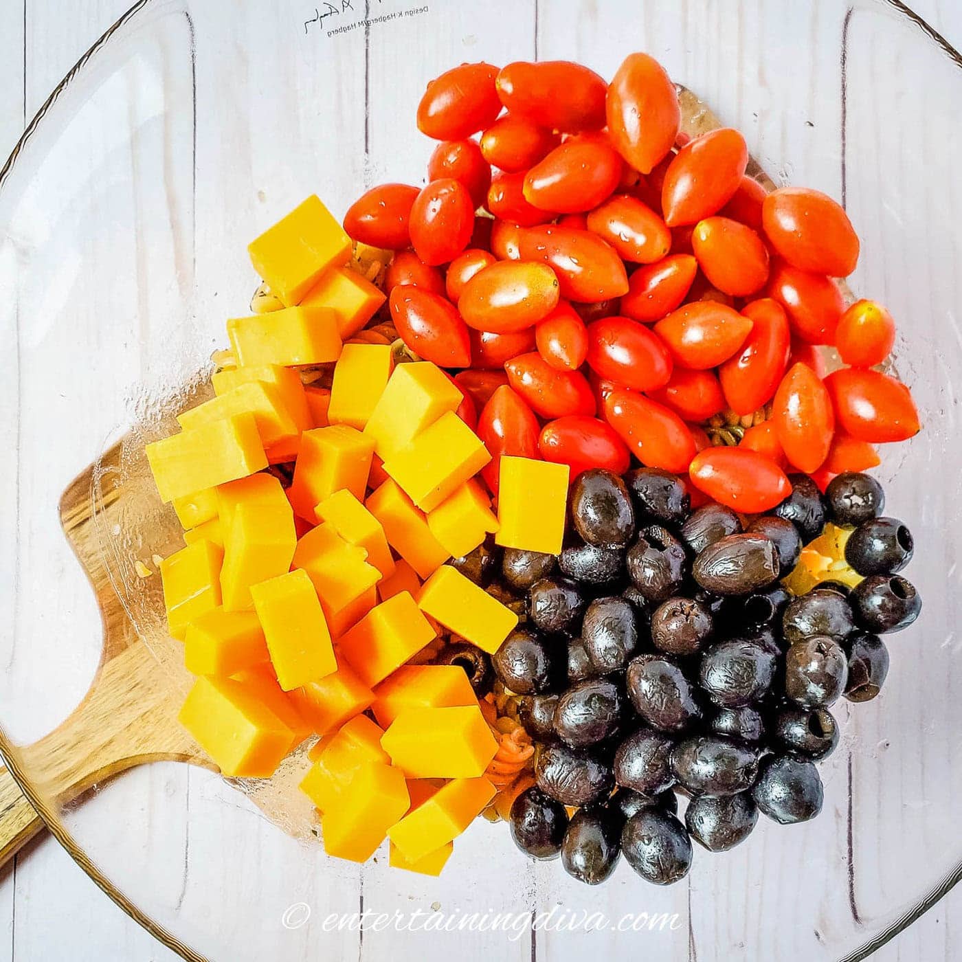 Chopped cheddar, washed cherry tomatoes and drained black olives in a bowl