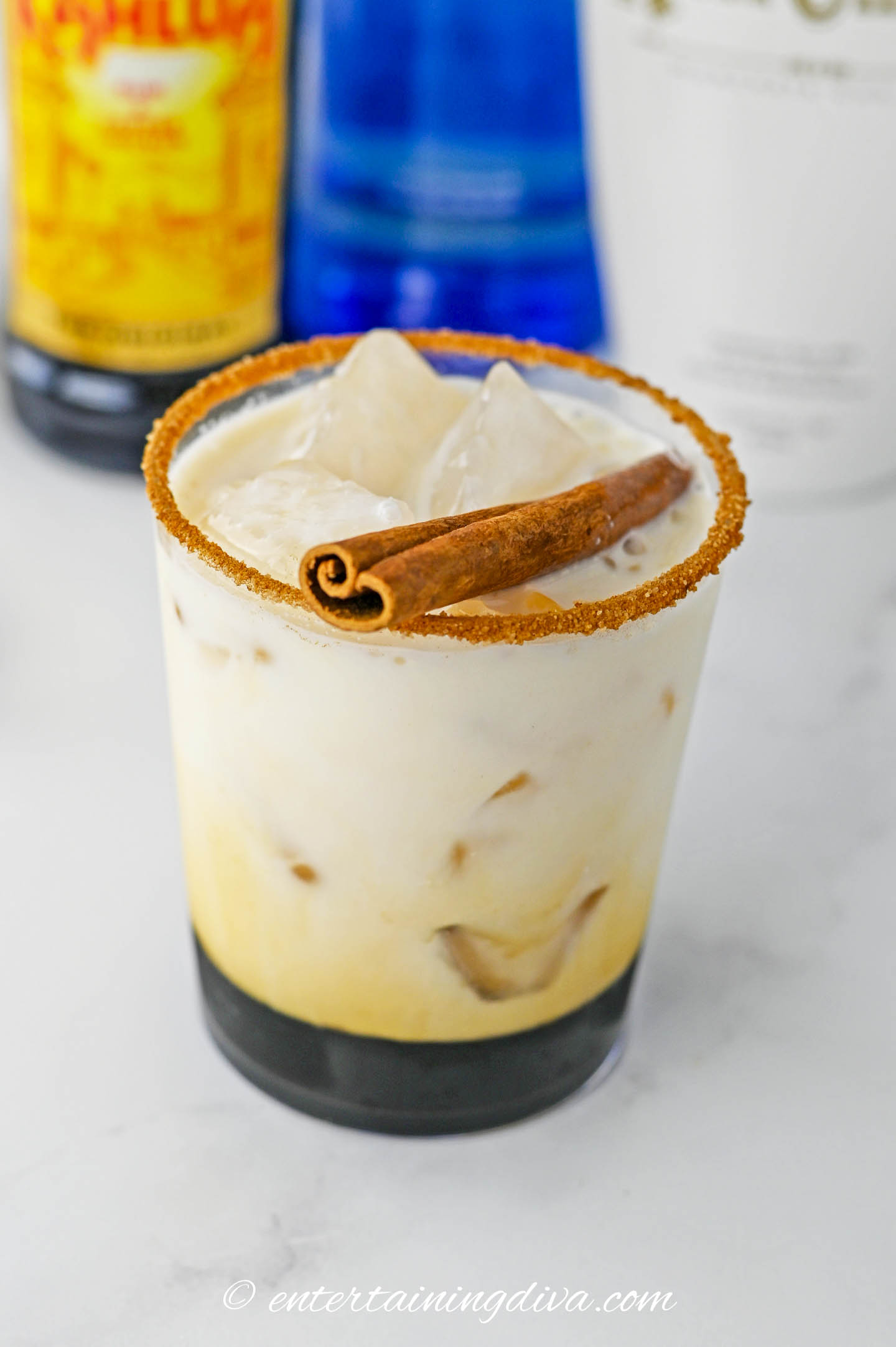 A cinnamon stick on top of a RumChata white Russian in a lowball glass