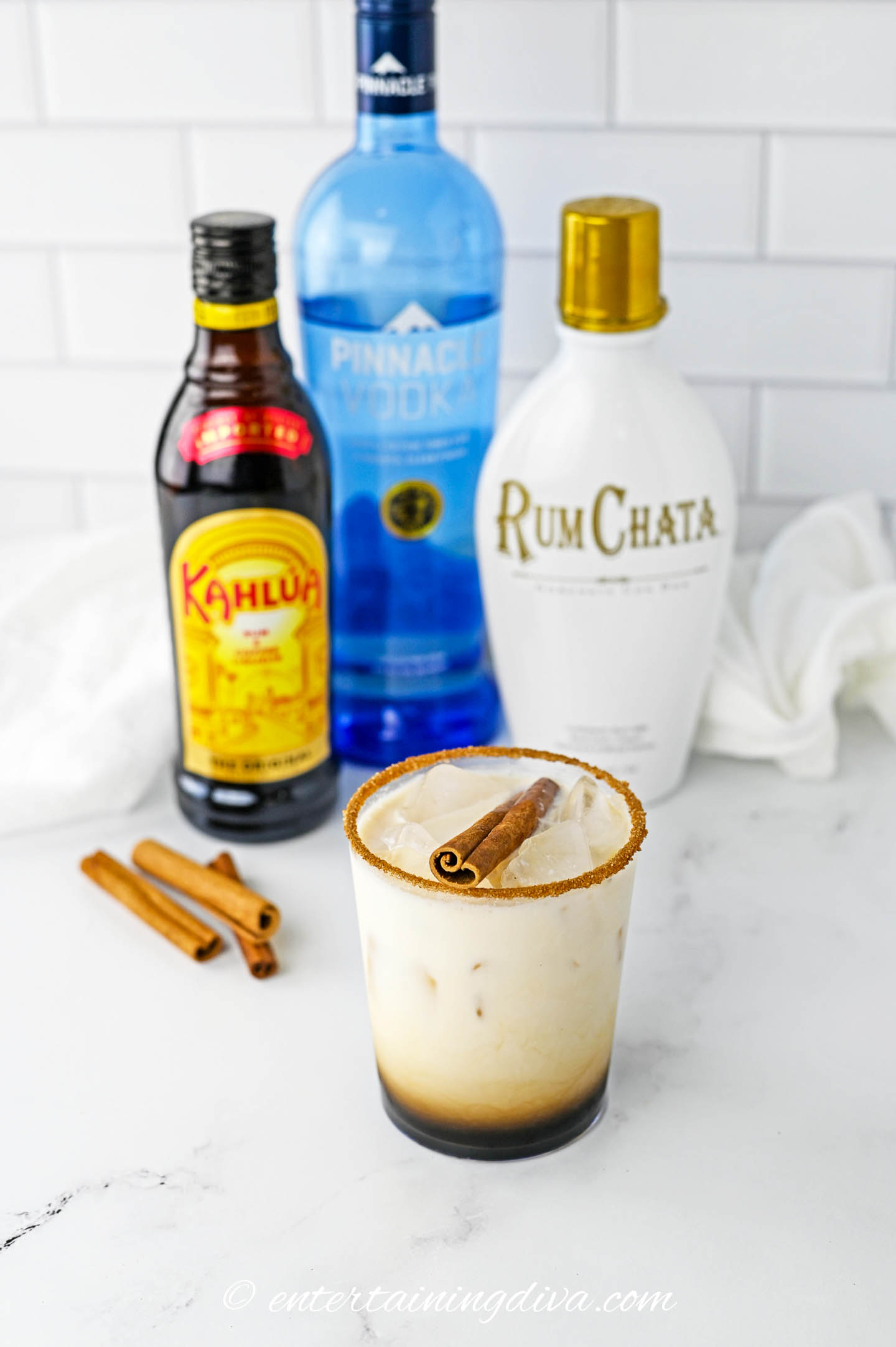 A RumChata white Russian in front of bottles of Kahlua, Vodka and RumChata