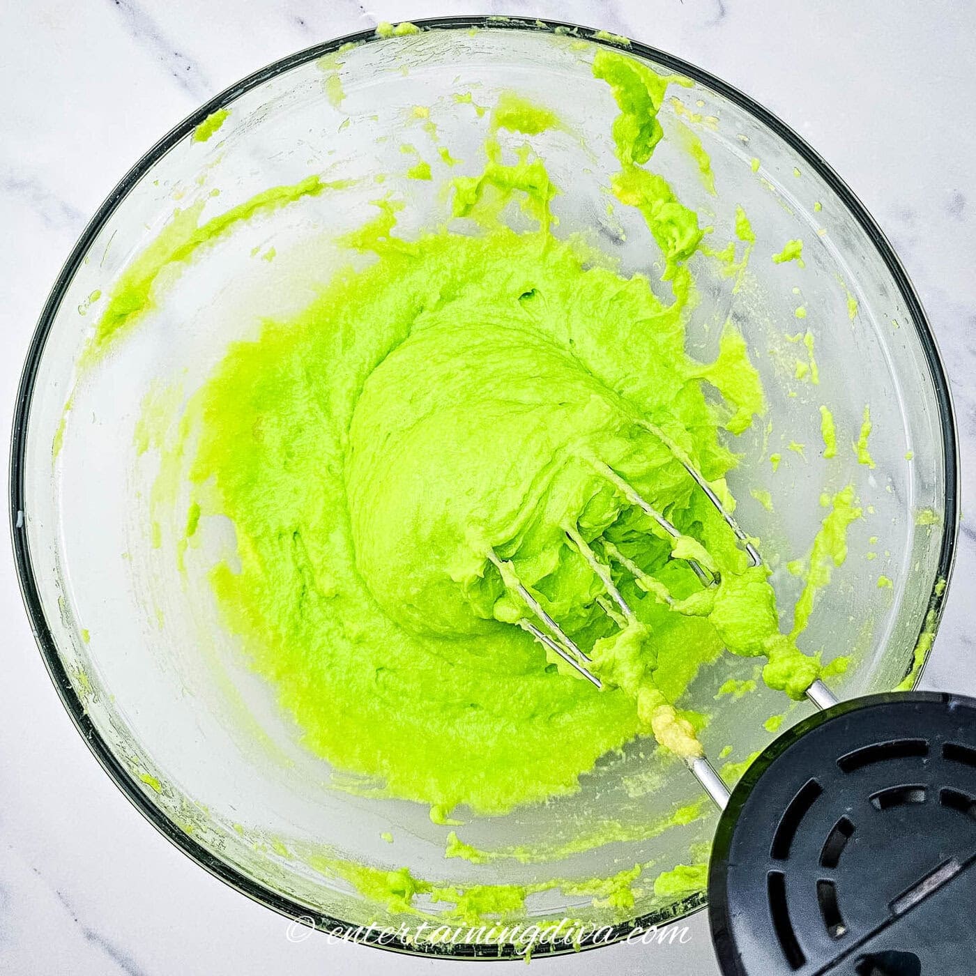 pudding mix with green food coloring in a mixing bowl with a mixer