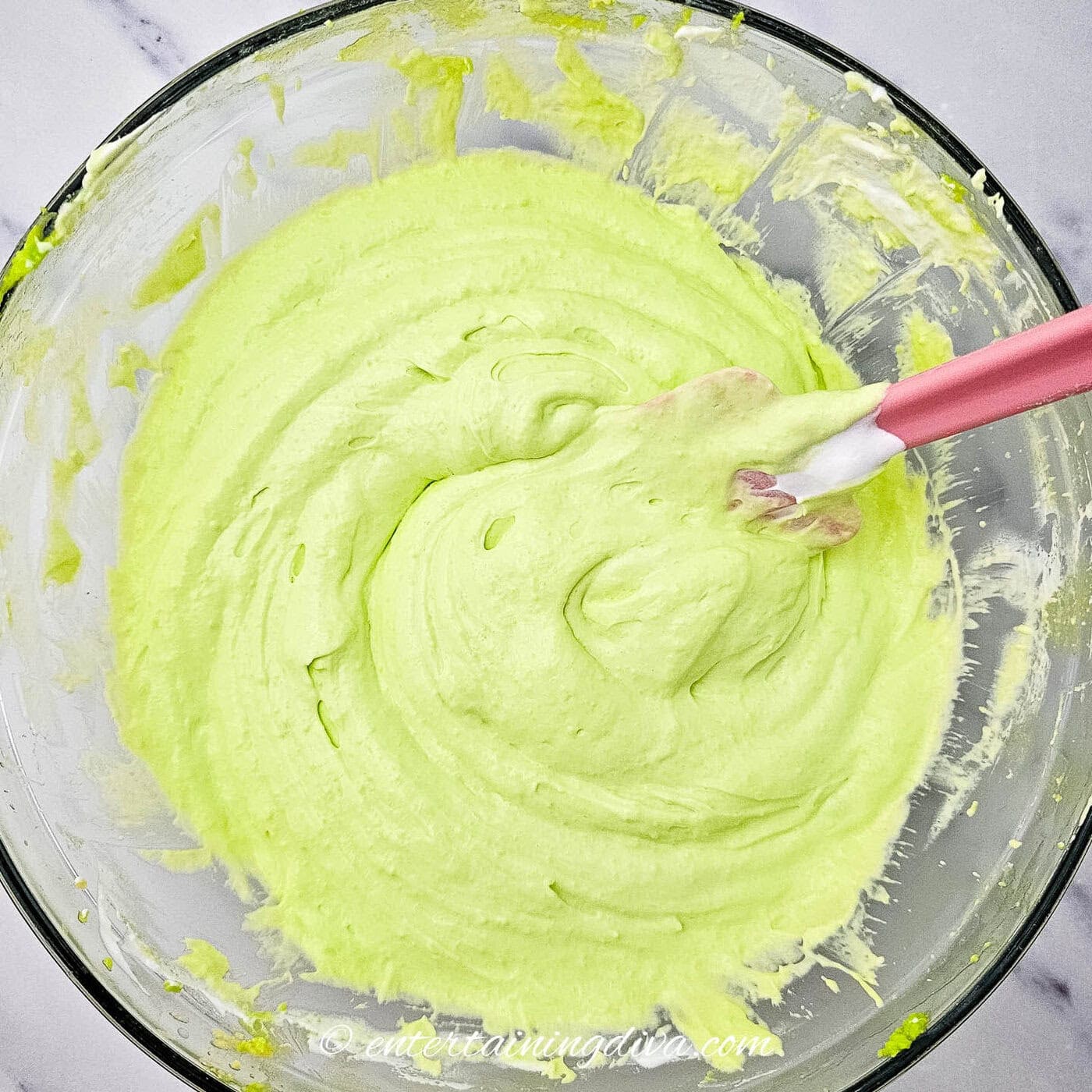 green pudding mix combined with cool whip in a bowl with a spatula