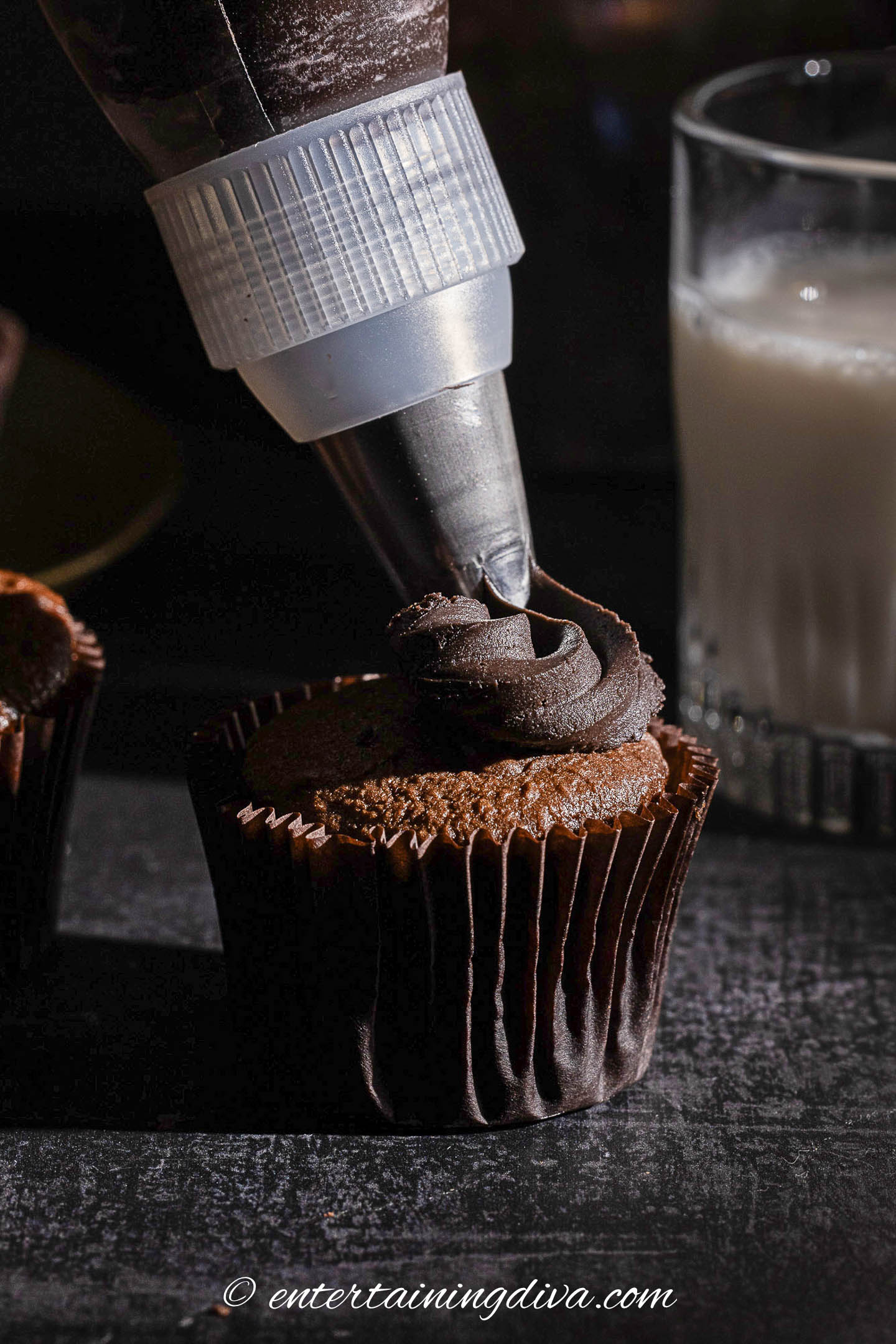 dark chocolate frosting being piped onto a chocolate cupcake