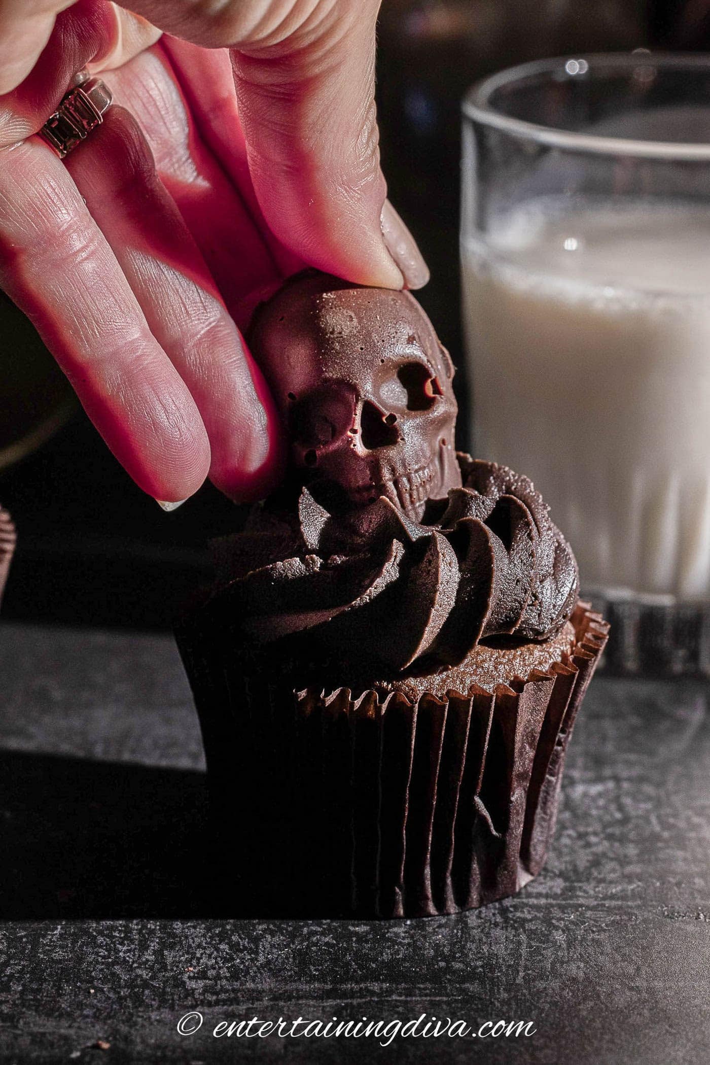 chocolate skull being added to the top of a chocolate cupcake
