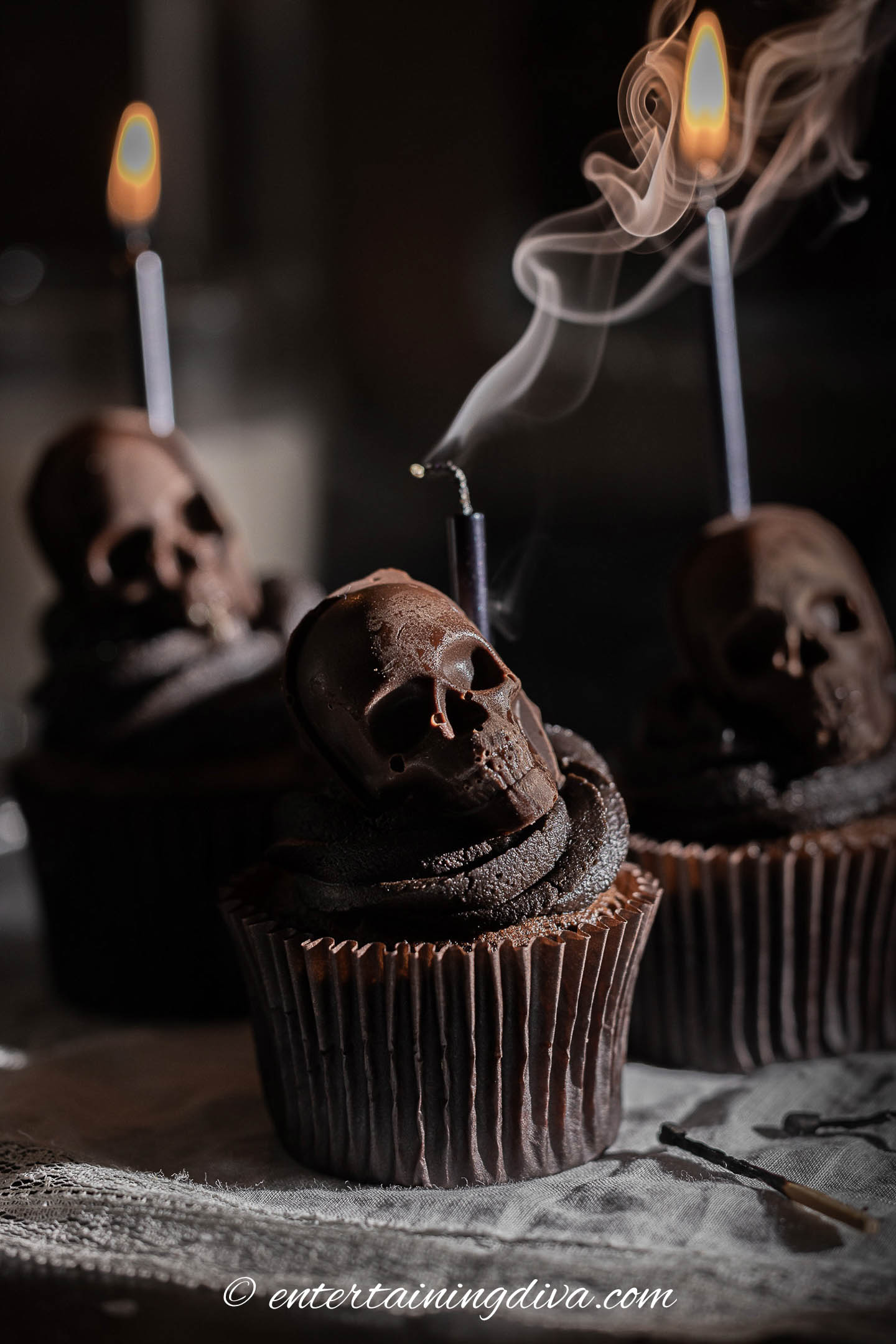 Three chocolate cupcakes with skulls and candles