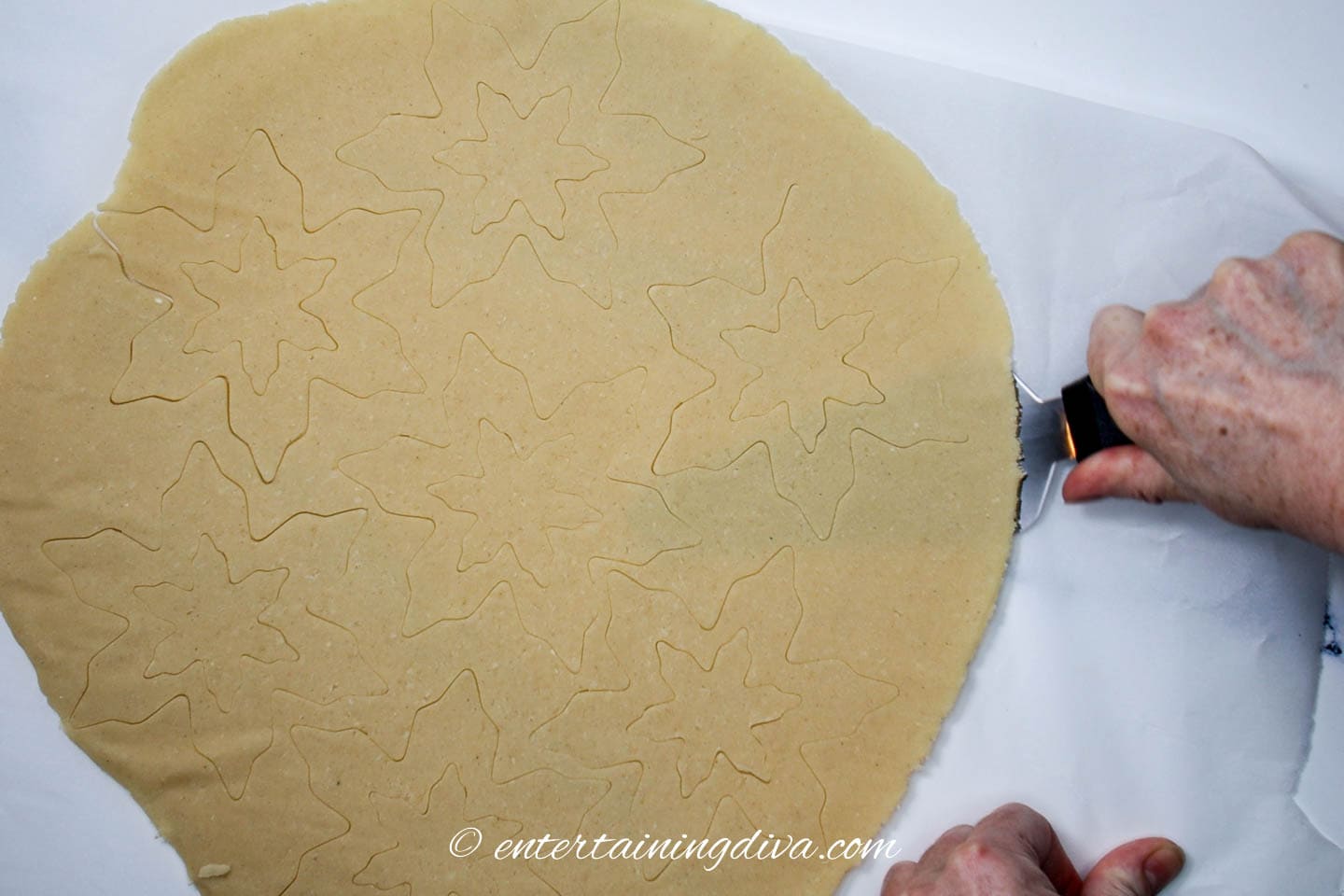 spatula removing parchment paper from rolled out cookie dough