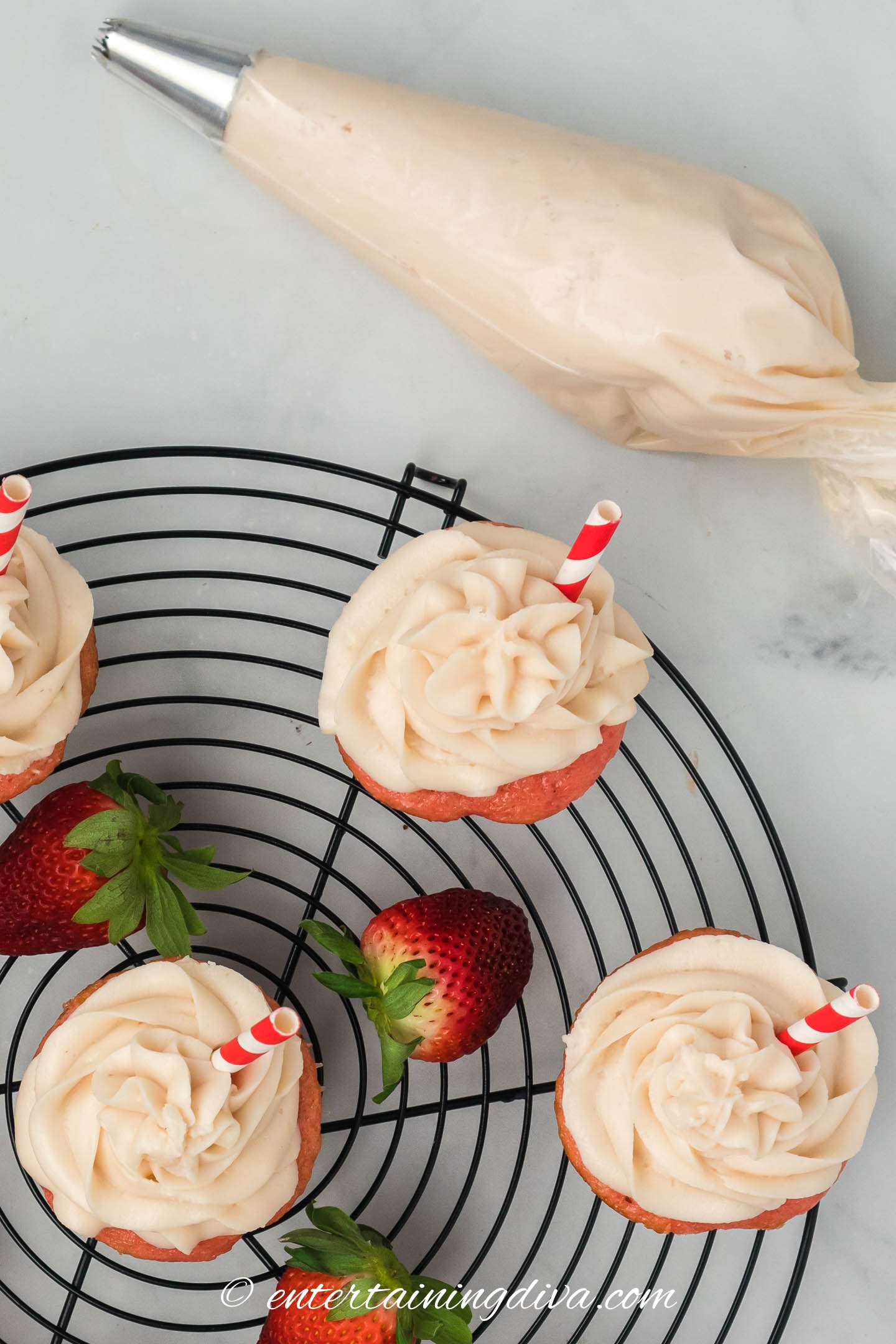 frosted soda cupcakes on a wire cooling rack beside a piping bag filled with cream cheese frosting