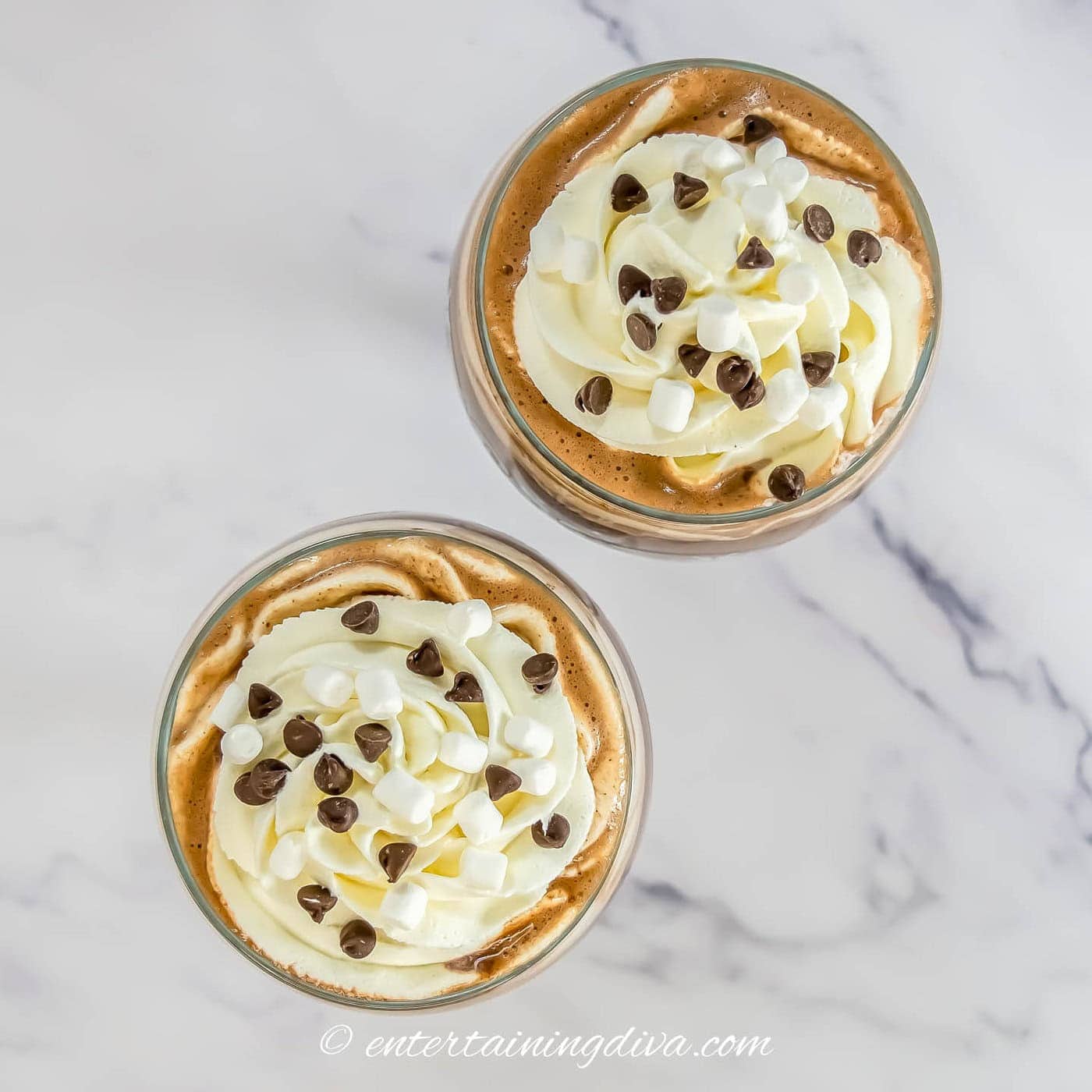 Overhead of 2 glasses of spiked peppermint hot cocoa garnished with whipped cream, mini marshmallows and mini chocolate chips