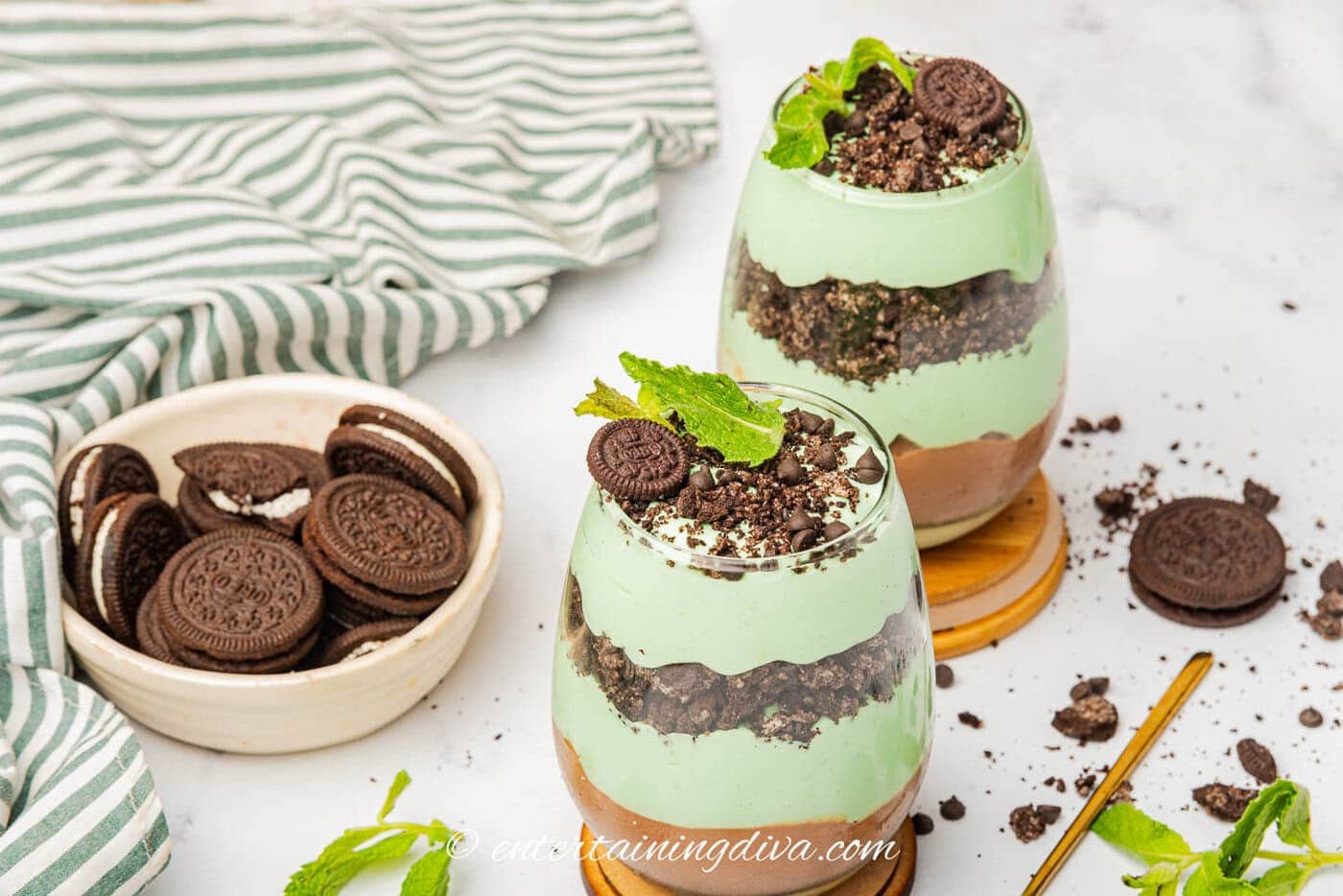 Two St Patrick's Day parfaits beside a bowl of Oreo cookies and a towel
