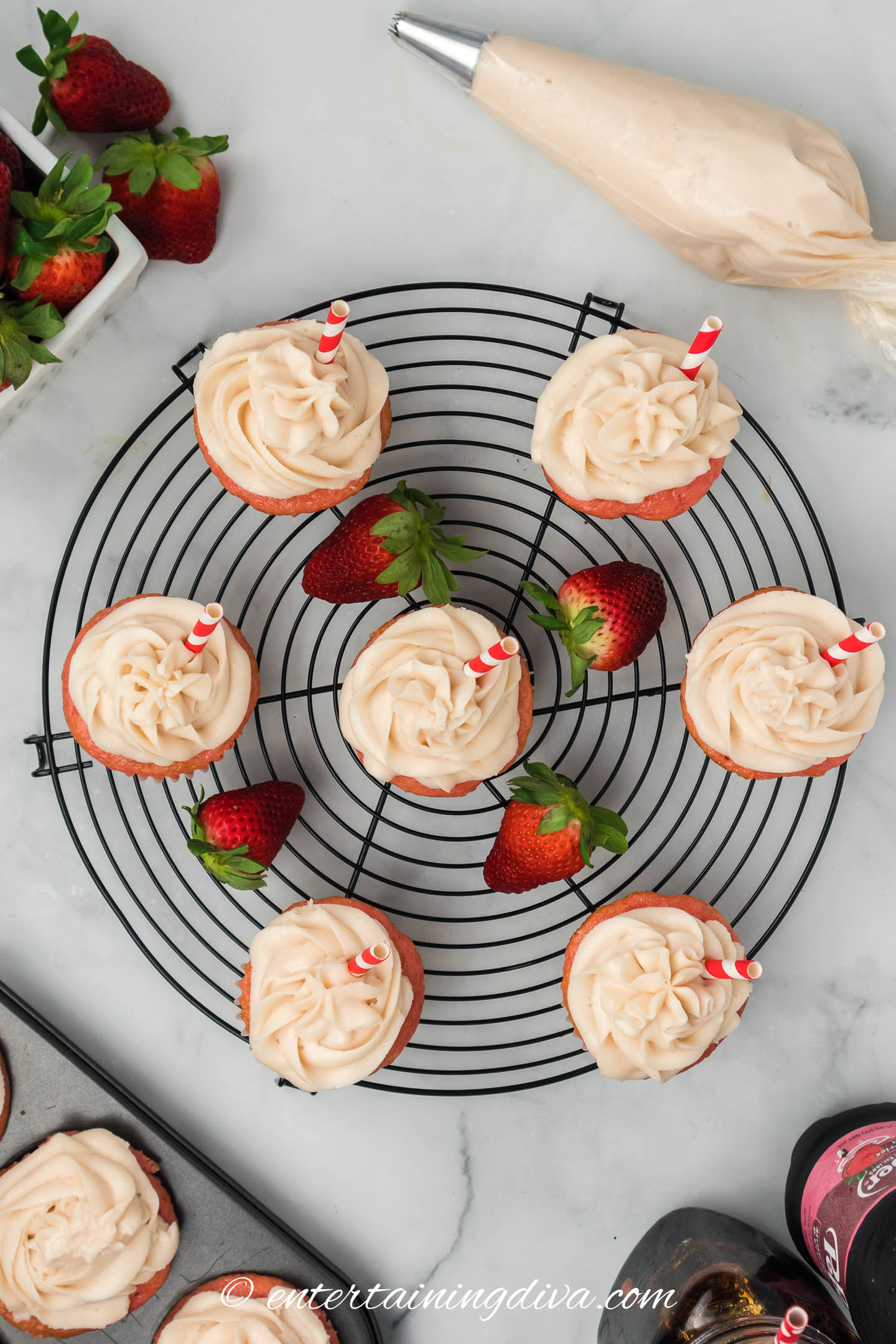 cupcakes with strawberry cream cheese frosting on a wire rack beside a bag of icing
