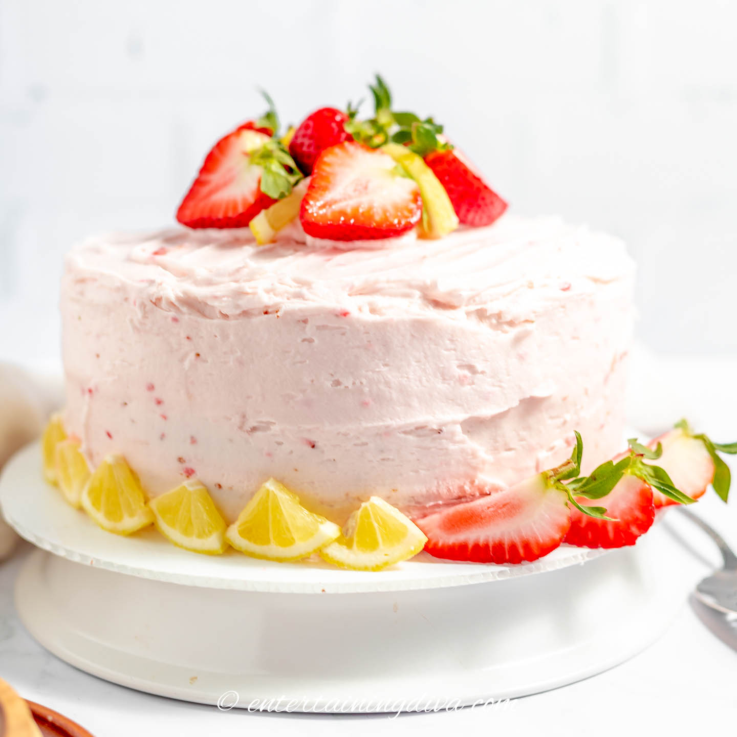 Side view of lemon cake with strawberry frosting garnished with strawberries and lemons