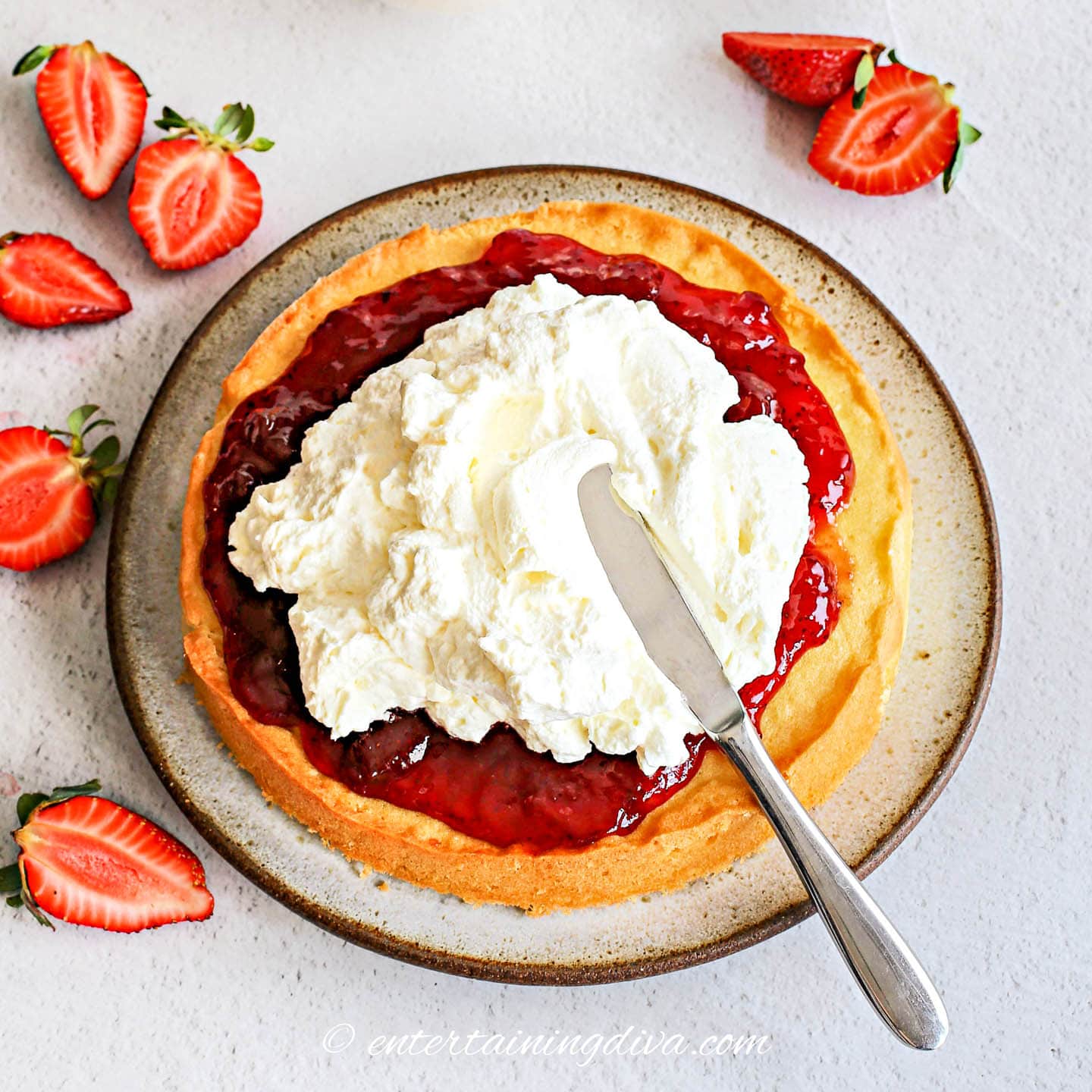 Bottom layer of strawberry shortcake cake spread with strawberry jam, fresh strawberries and whipped cream