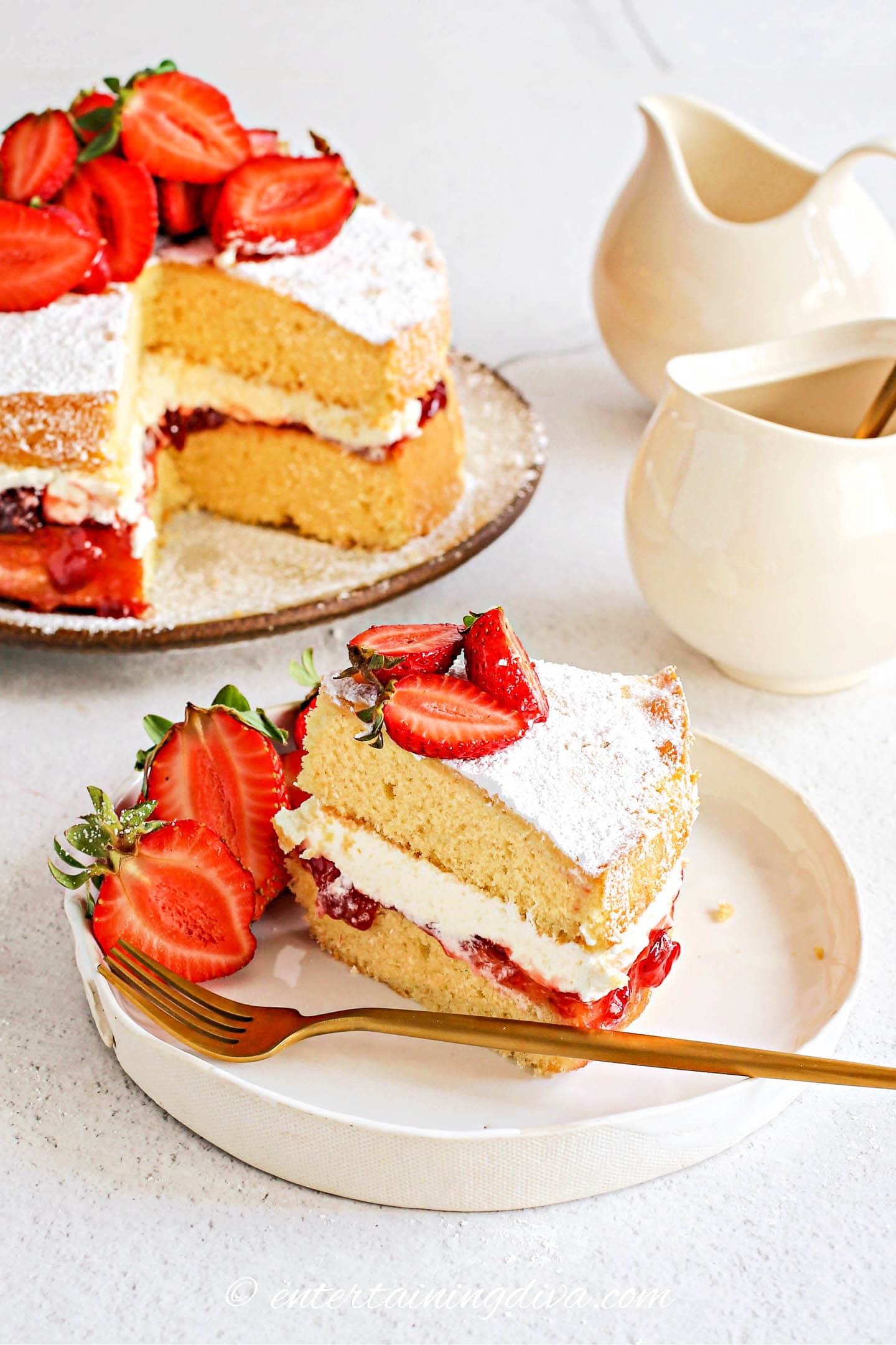 A piece of strawberry shortcake cake on a plate in front of the rest of the cake