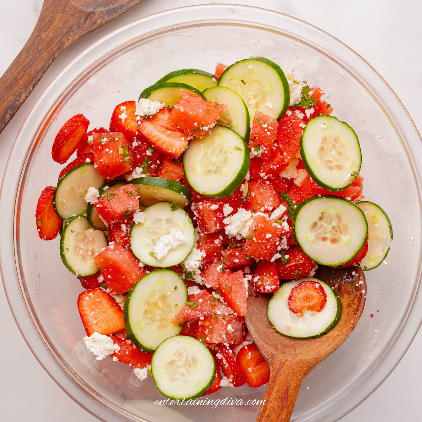 strawberry watermelon cucumber salad being mixed in a bowl with a wooden spoon