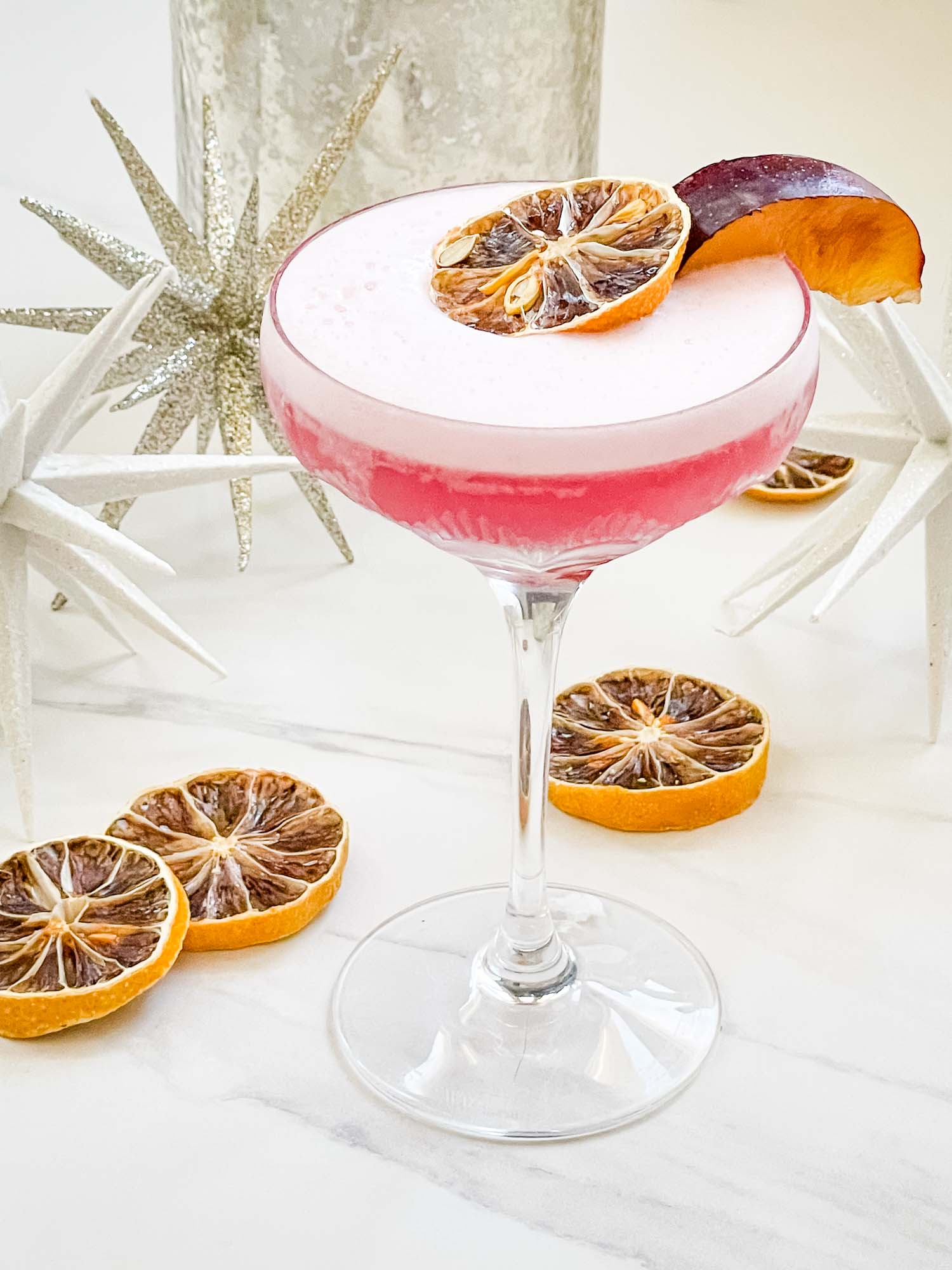 A martini with a pink drink and orange slices.