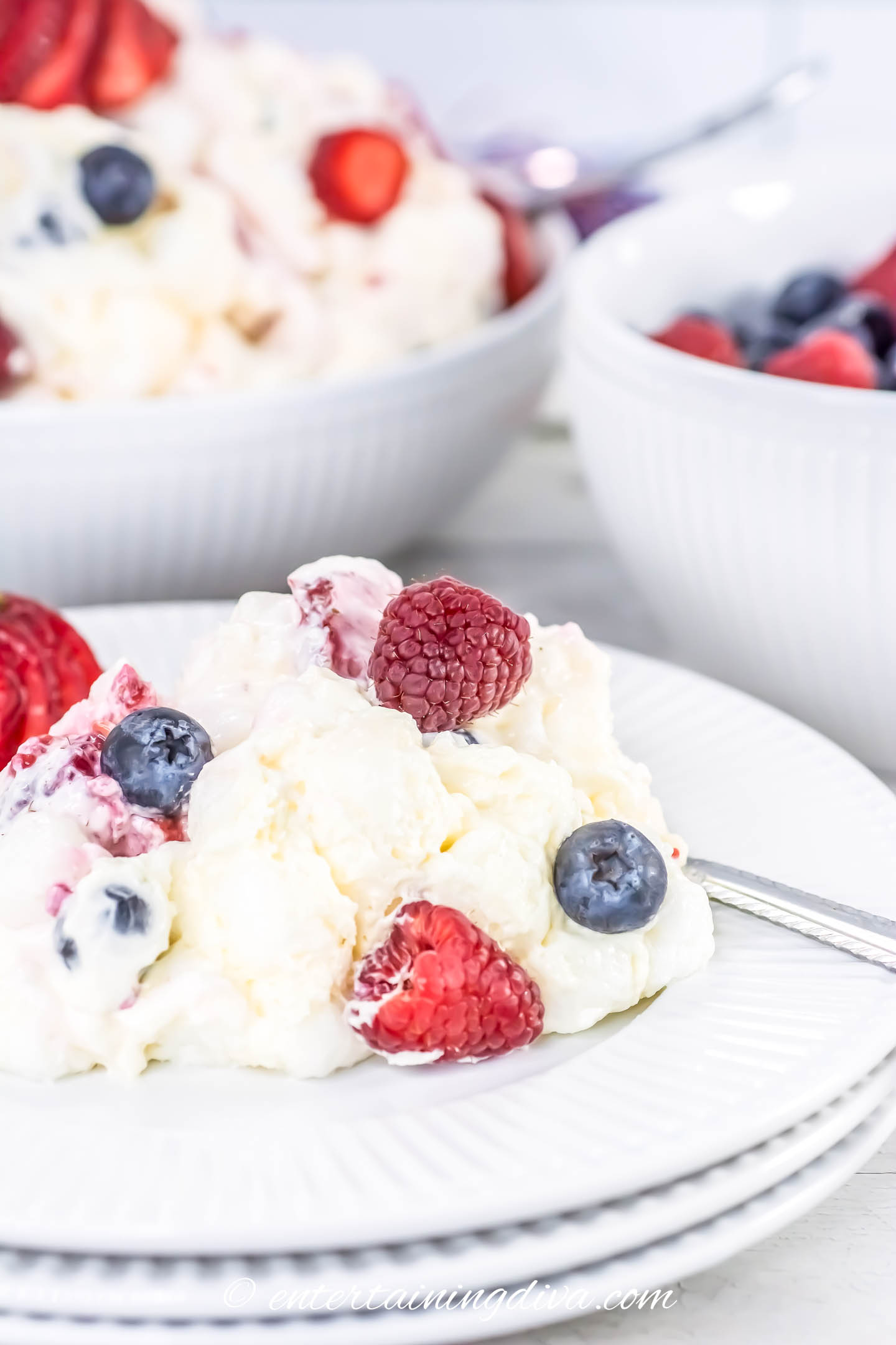 A plate of creamy dessert topped with fresh raspberries and blueberries, with bowls of similar dishes in the background.