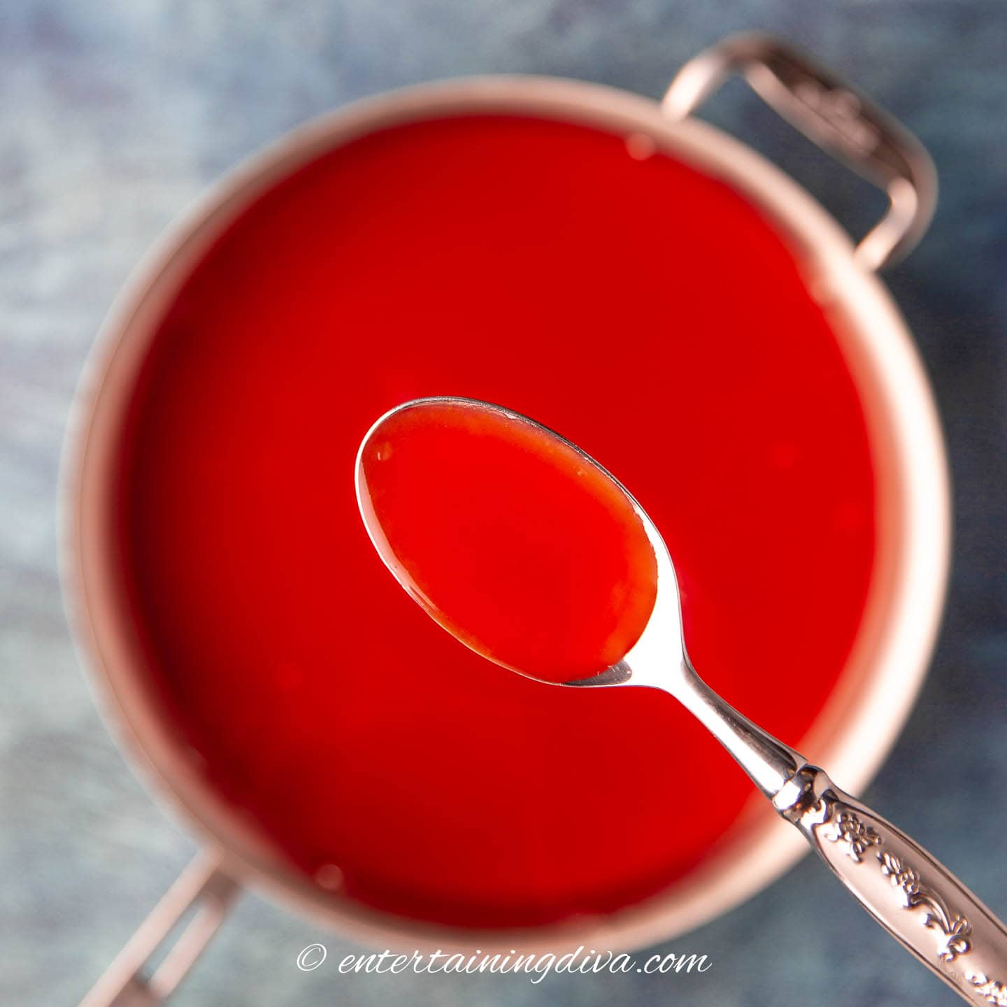 A spoon with thickened sweet and sour sauce above a saucepan