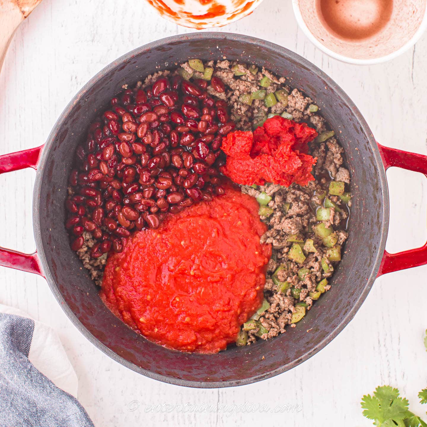 beans and tomatoes on top of browned ground beef and bell peppers in a dutch oven