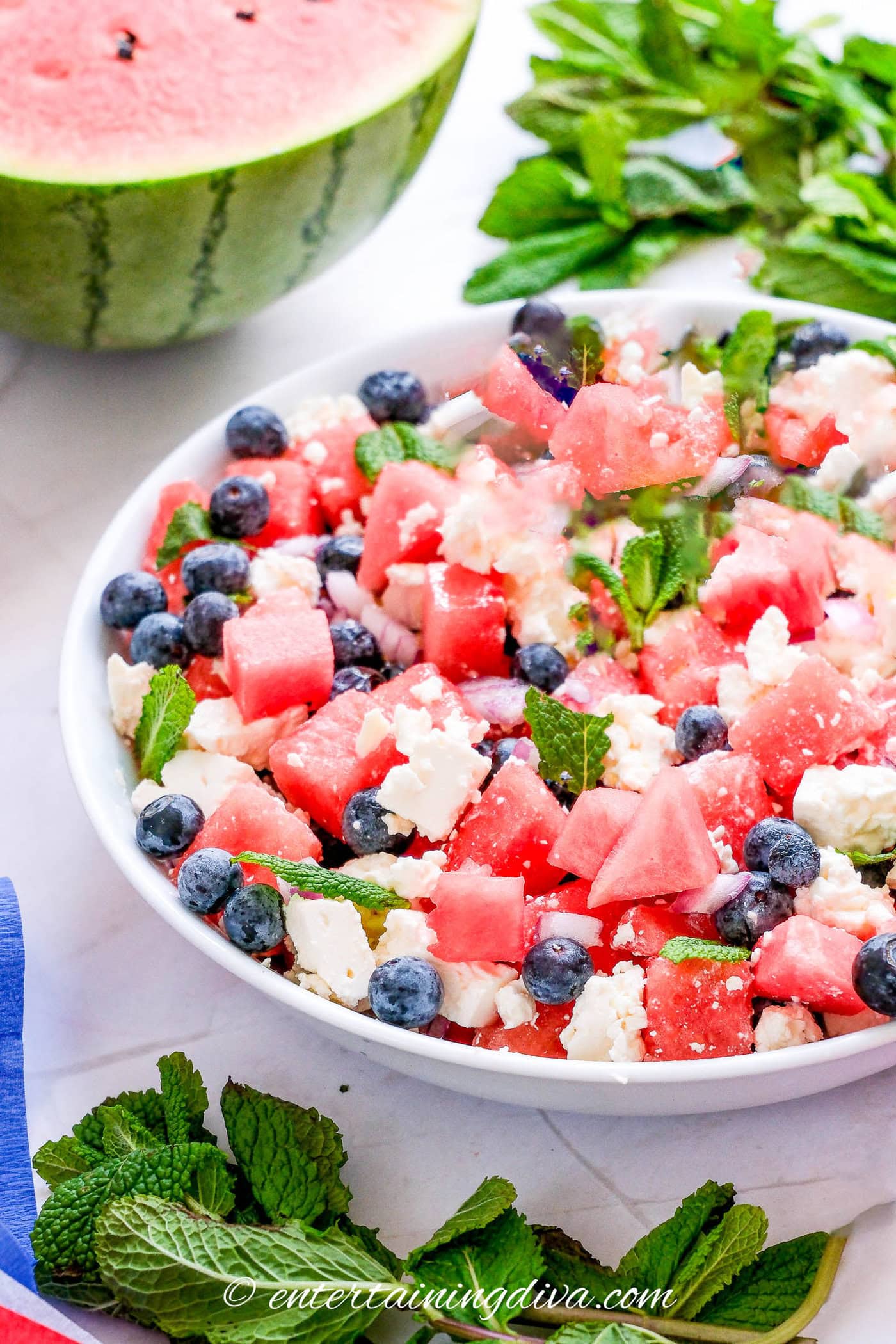 watermelon feta salad in a bowl beside mint leaves and half a watermelon