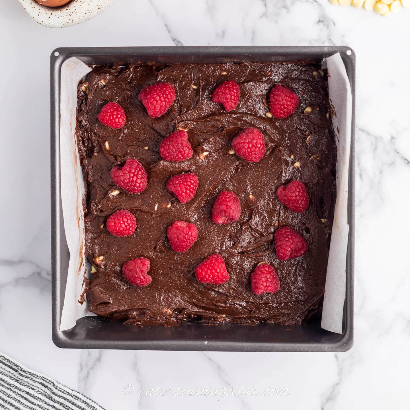 fresh raspberries sprinkled on top of brownie batter in a square baking pan