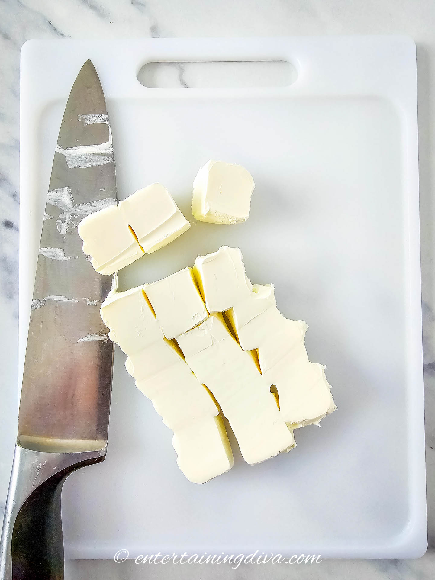Cream cheese chopped into cubes on a cutting board with a knife