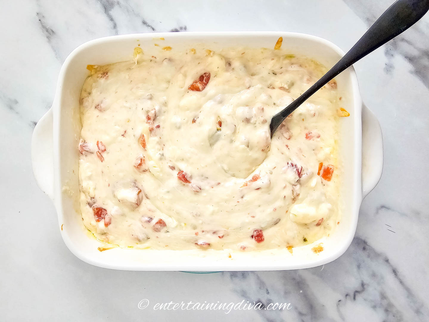 white queso being stirred in a baking dish
