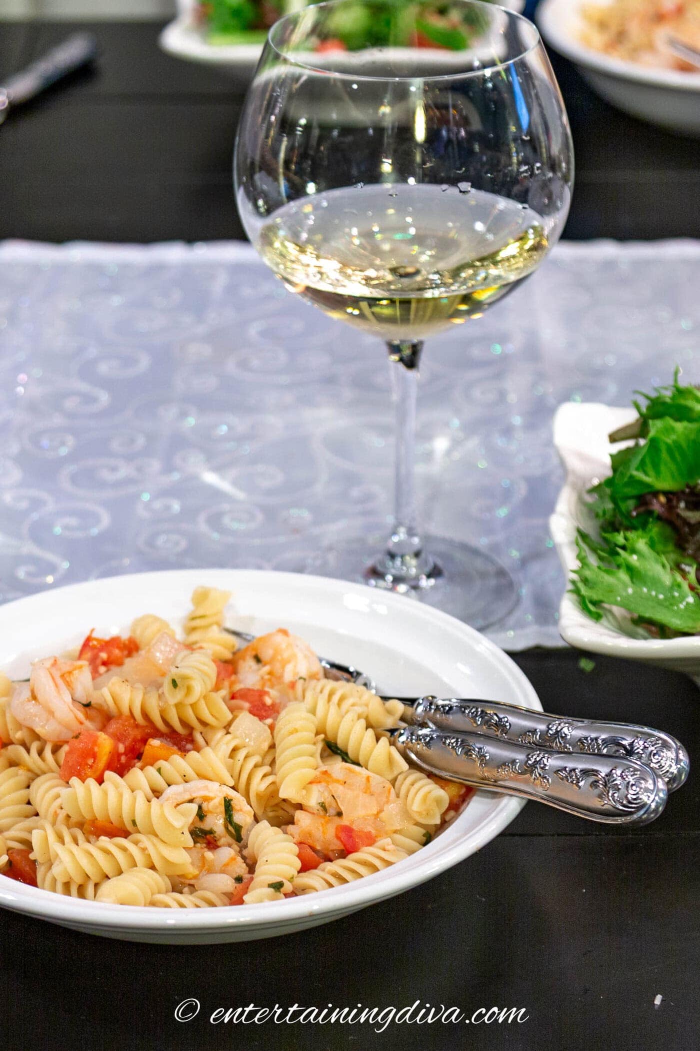 white Wine Lemon Herb Shrimp Rotini in a bowl with a glass of wine and salad in the background