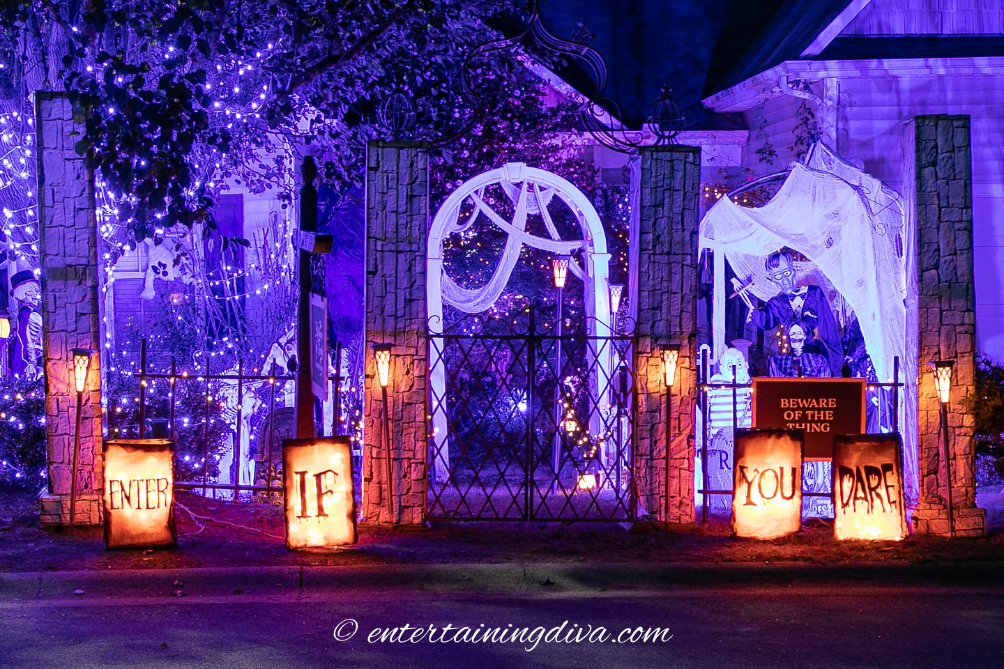 A house decorated for Halloween with purple lights, cobwebs, skeletons, and illuminated signs that read "ENTER IF YOU DARE.