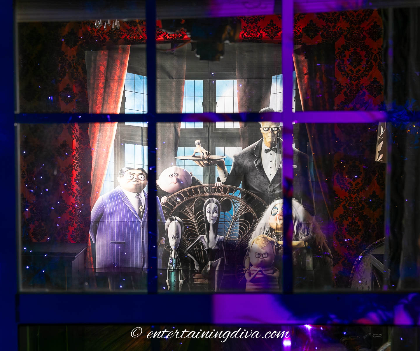 A window display shows life-sized figures of the Addams Family, including Gomez, Morticia, Lurch, Wednesday, Pugsley, and Uncle Fester, with gothic decor and dramatic lighting.