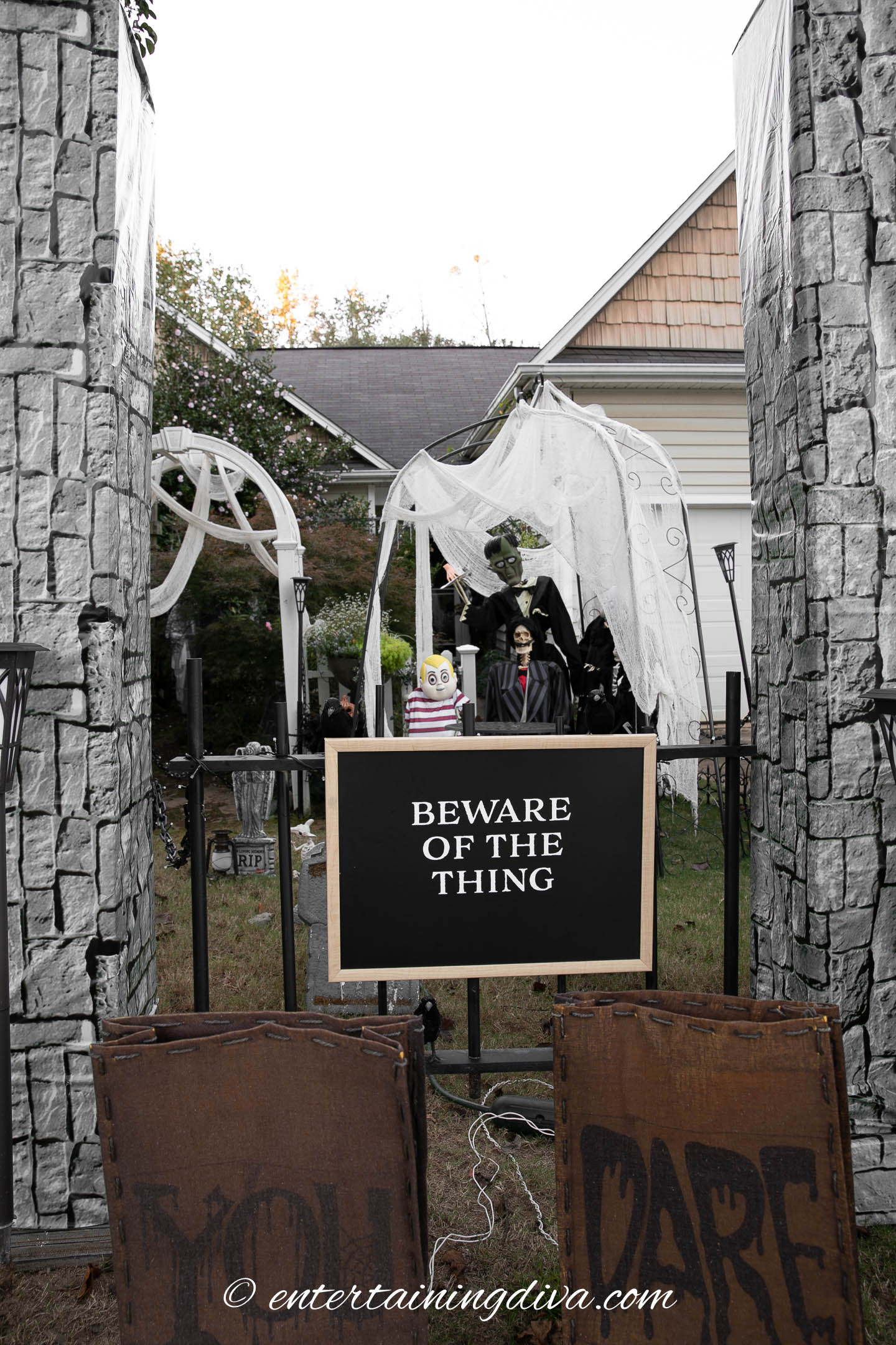 A Halloween yard display features a sign reading "BEWARE OF THE THING," with spooky decorations and skeletons in front of a house.