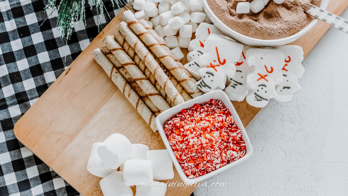 hot chocolate mix in a bowl with marshmallows, wafer cookies, and crushed candy canes in a bowl