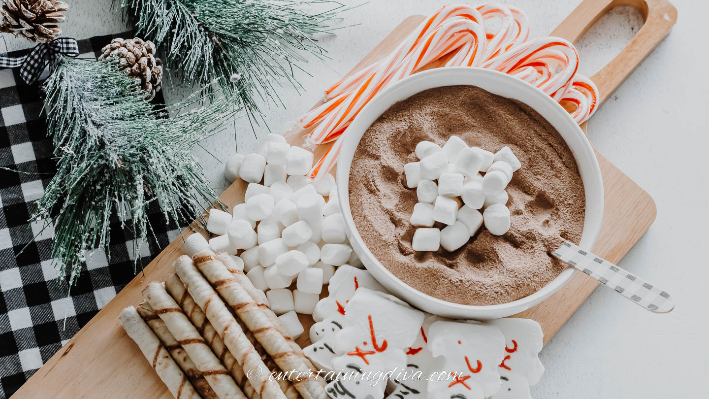 hot chocolate mix in a bowl, marshmallows, snowman peeps, candy canes and wafer cookies on a cutting board