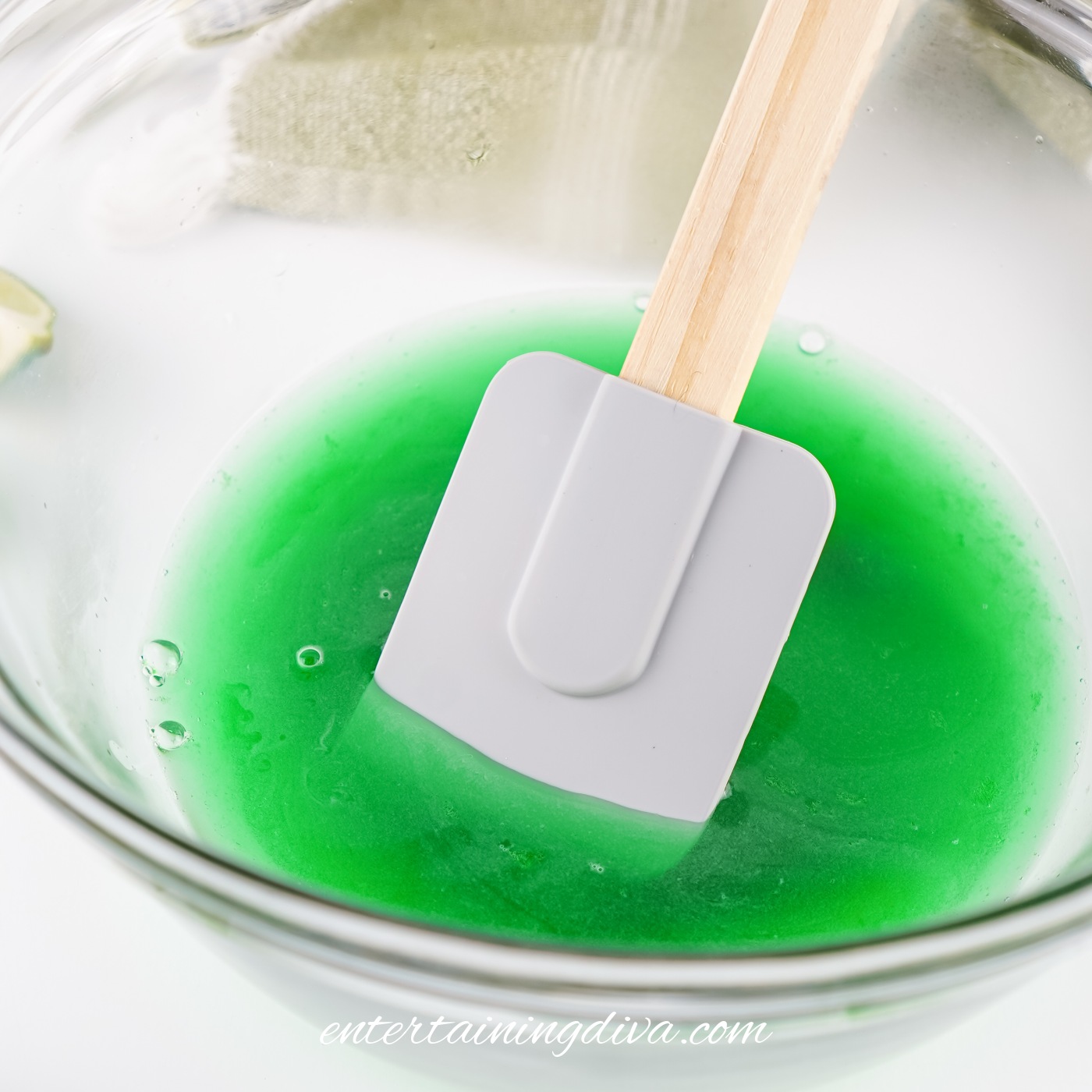 A white spatula rests in a glass bowl containing lime Jello.