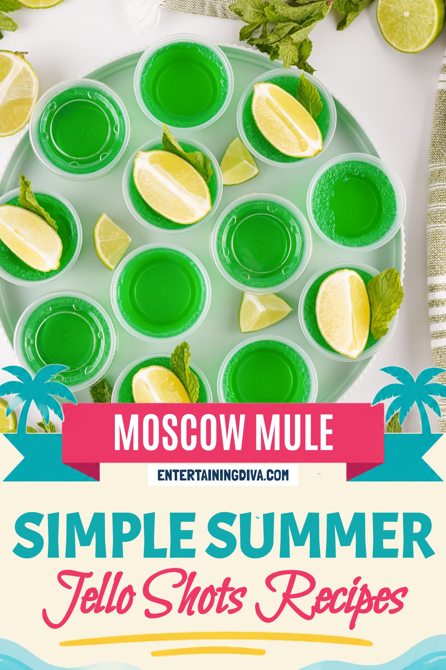 Overhead view of a round tray with green Moscow Mule Jello shots in plastic cups, garnished with a lime wedge and fresh mint; extra limes and mint scattered around.