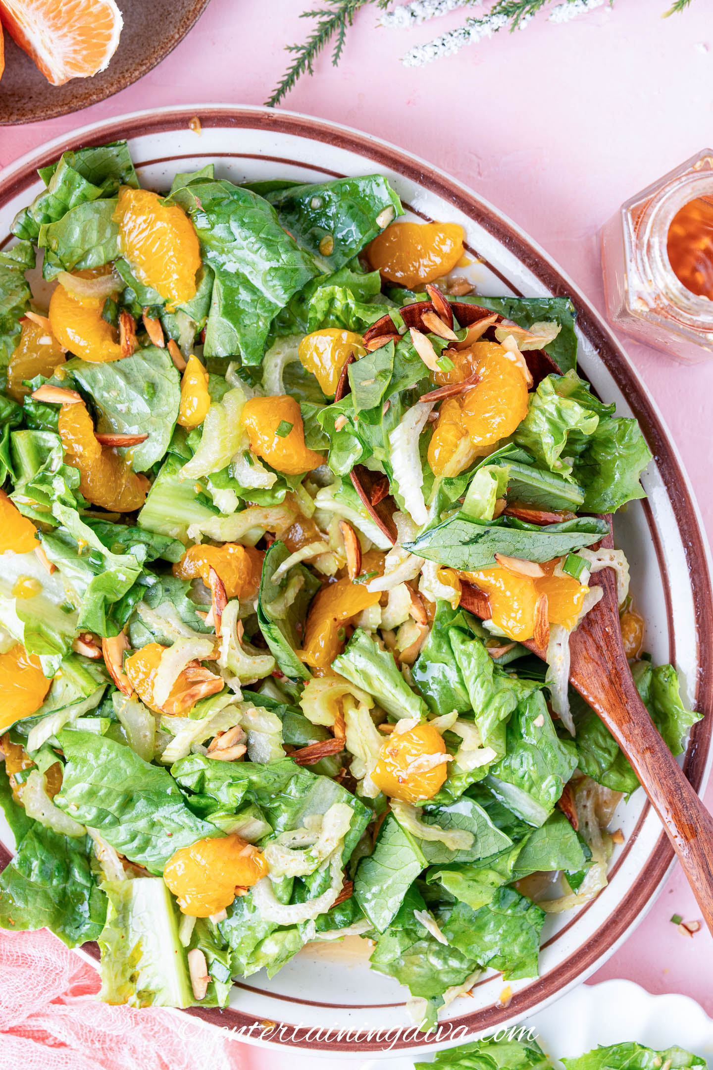 A bowl of green salad with romaine lettuce, mandarin orange segments, sliced almonds, and a wooden serving spoon.