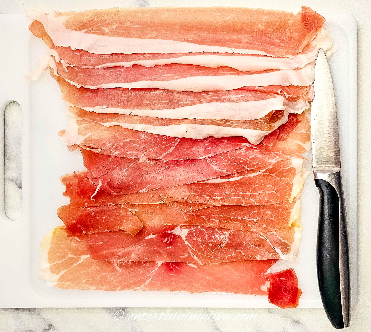 slices of prosciutto on a cutting board with a knife