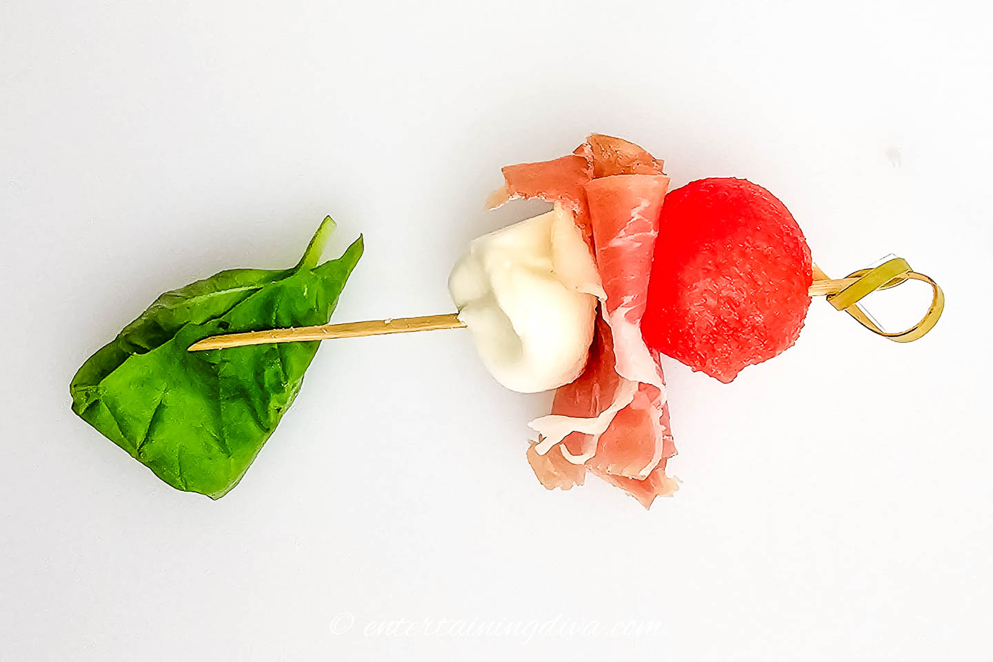 A folded basil leaf being threaded onto a watermelon prosciutto skewer