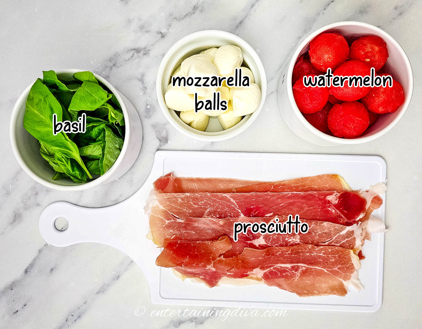 basil, mozzarella balls, watermelon and prosciutto on a white countertop