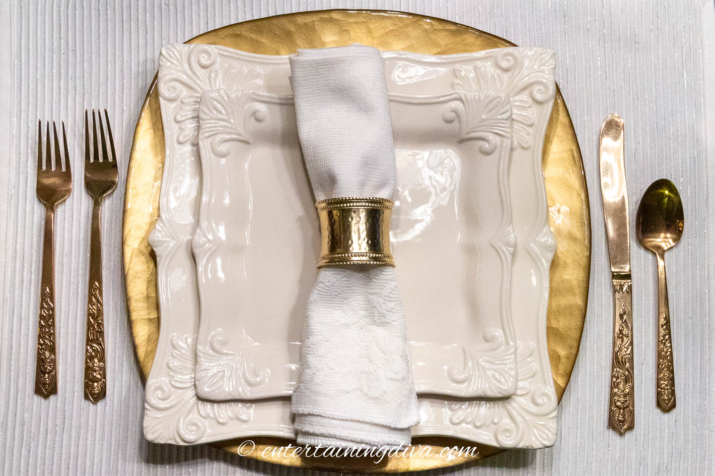 white dishes and napkin with gold cutlery and napkin ring on a gold charger