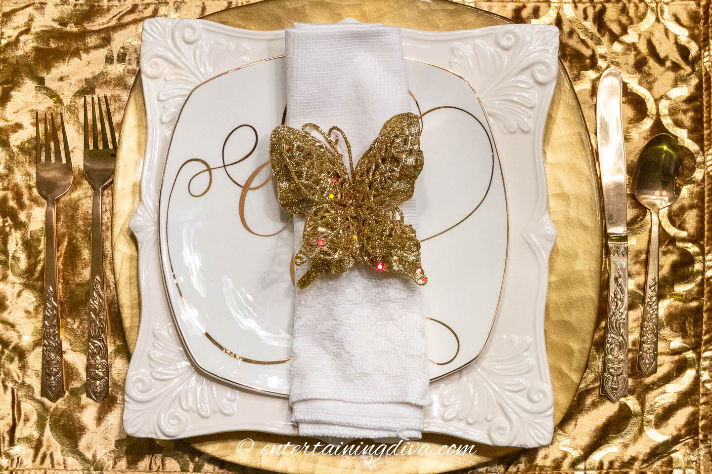 White dinnerware on a gold charger and place mat with a gold butterfly napkin ring