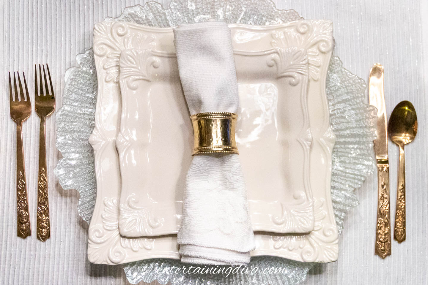 A white monochromatic table setting with gold cutlery and napkin ring