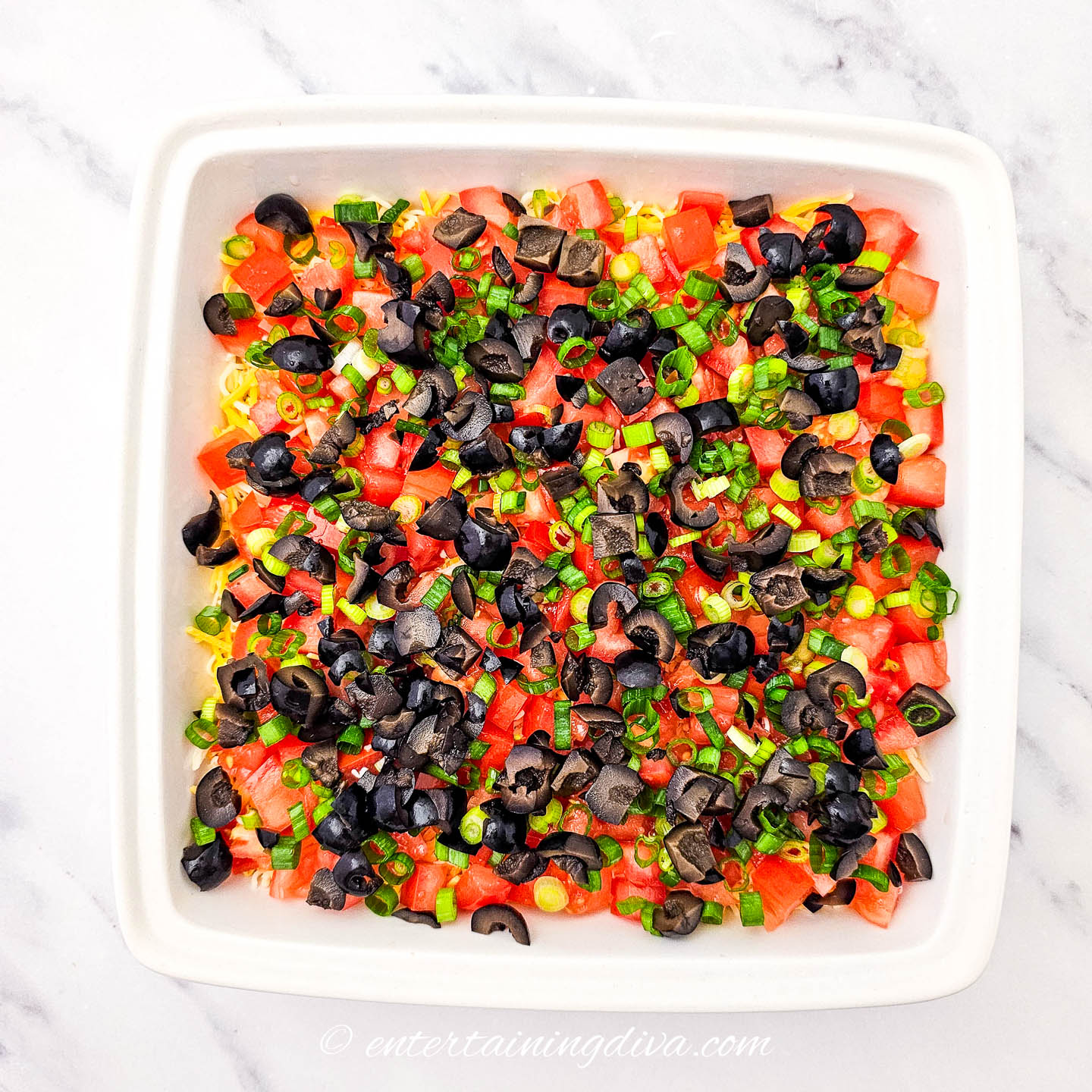black olives, chopped green onions, and diced tomatoes on top of a 7-layer dip