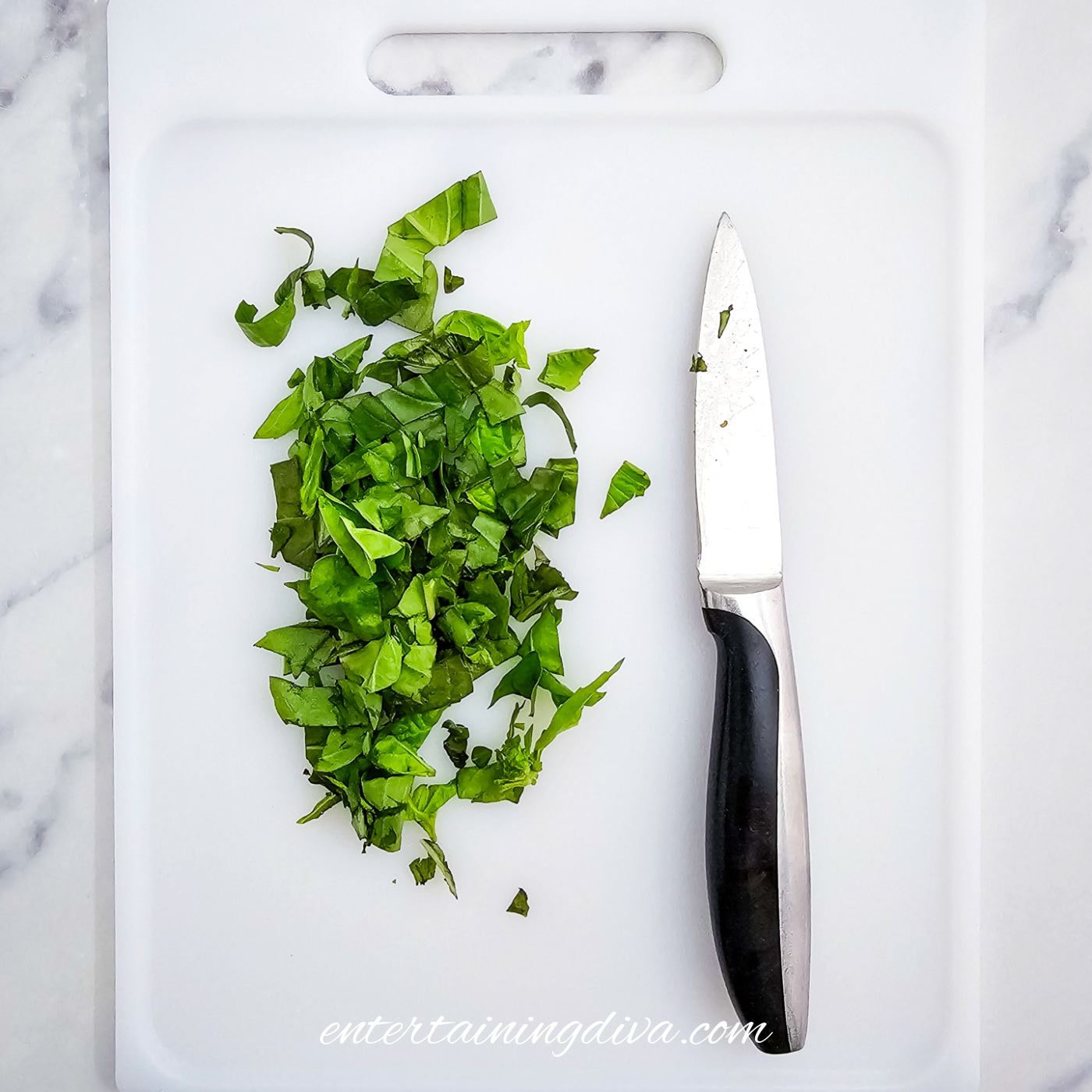 chopped basil on a white cutting board with a knife