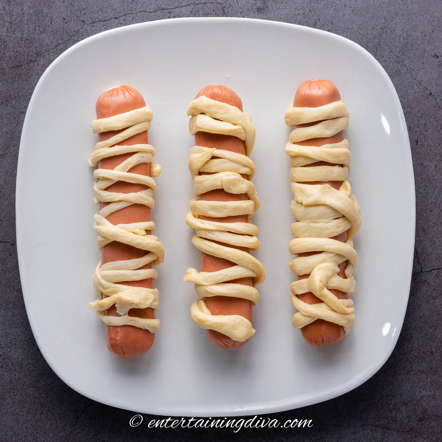 weiners wrapped with strips of crescent roll dough on a plate