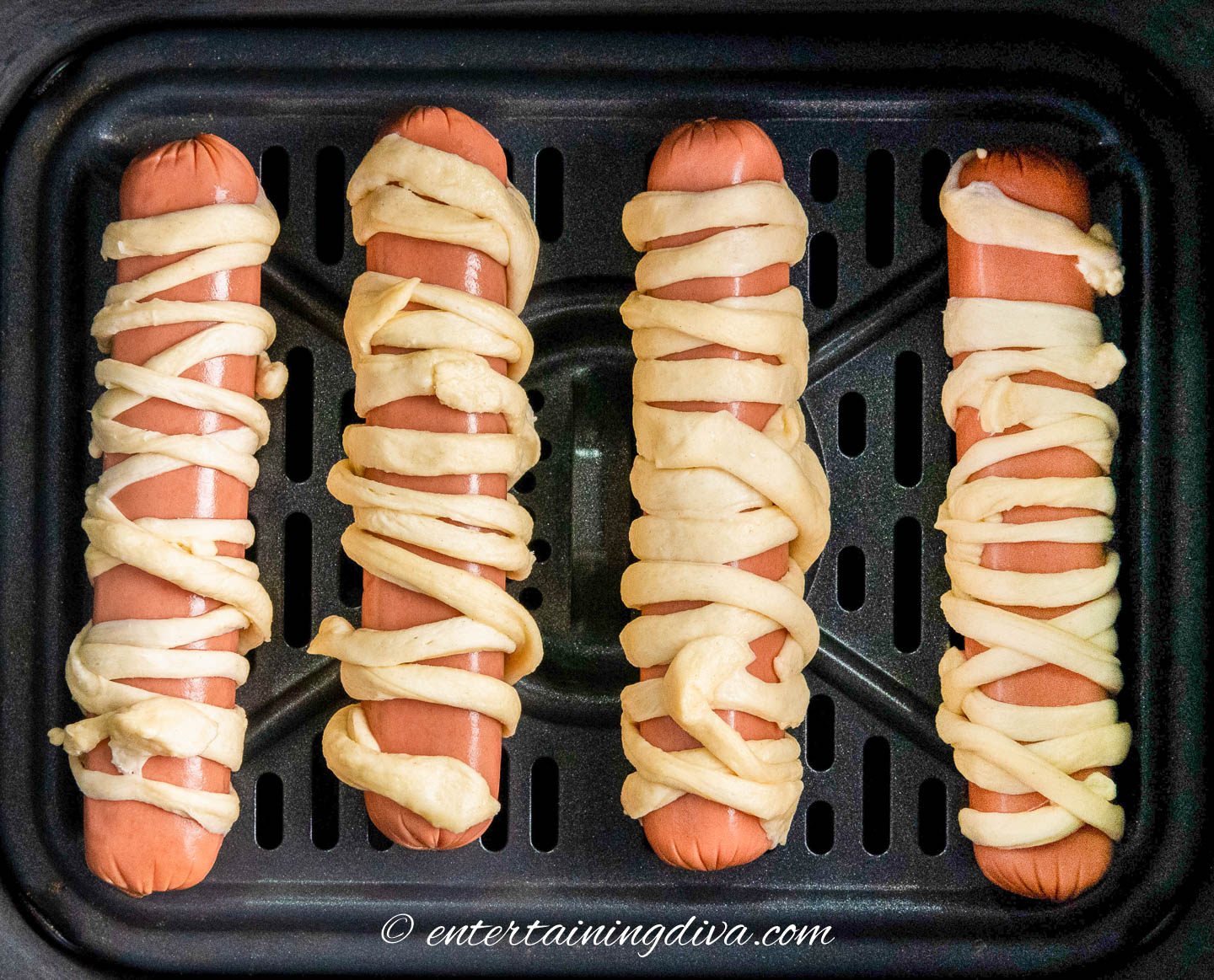 4 weiners wrapped in crescent roll dough on a baking sheet