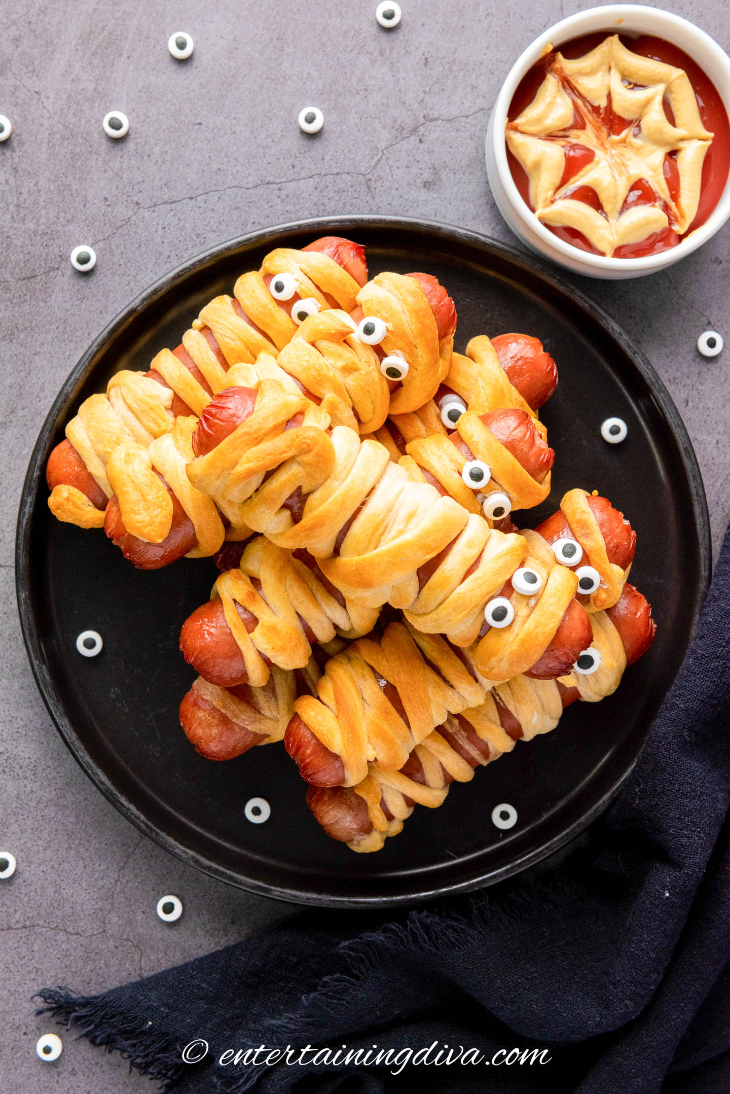An overhead view of a plate of Halloween mummy dogs with a bowl of ketchup in the corner