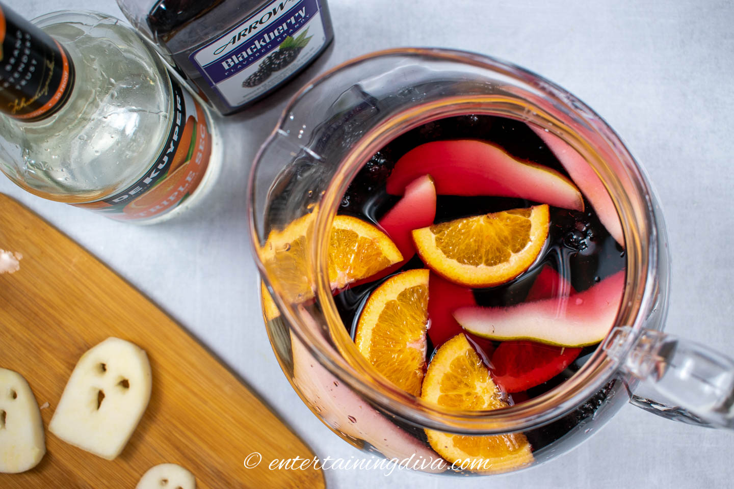 A pitcher of blackberry Halloween sangria beside a cutting board with pear ghosts