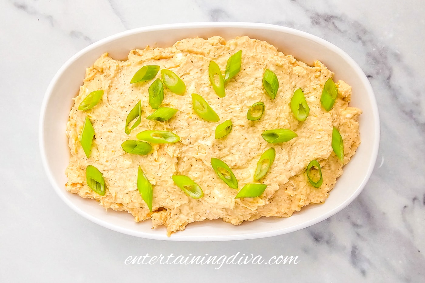 Crab dip with cream cheese topped with sliced green onions in a baking dish before being baked